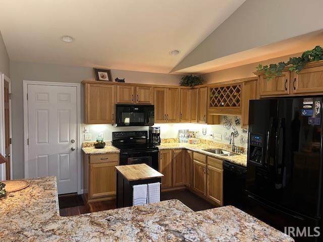Kitchen featuring black appliances, lofted ceiling, light stone counters, and brown cabinets