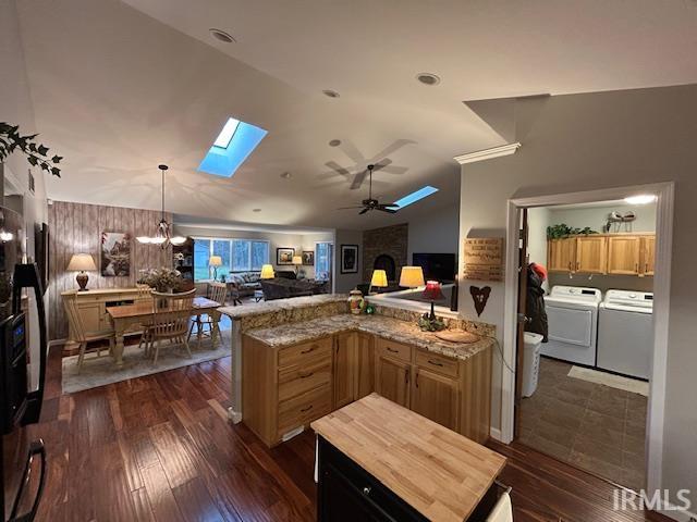 Kitchen featuring vaulted ceiling, open floor plan, a skylight, hanging light fixtures, and dark wood-style flooring