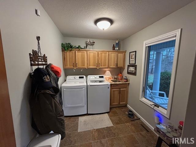 Washroom with a textured ceiling, cabinet space, and washing machine and dryer
