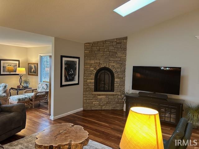 Living area featuring wood finished floors, lofted ceiling, and a stone fireplace