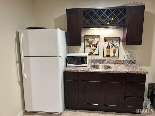 Kitchen featuring white appliances, dark brown cabinetry, and light stone counters