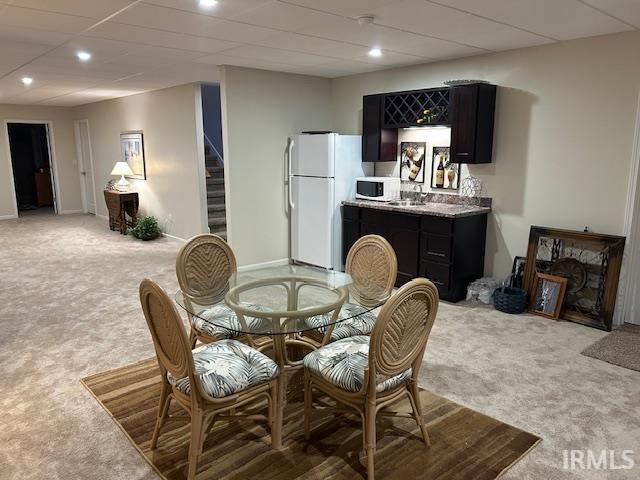 Dining area featuring light carpet, stairway, bar with sink, and a paneled ceiling