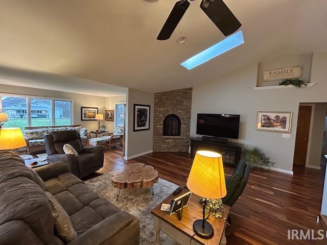 Living room featuring vaulted ceiling, dark wood-type flooring, a fireplace, a ceiling fan, and a skylight