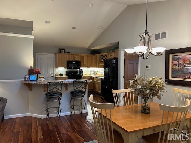 Kitchen featuring brown cabinetry, a kitchen breakfast bar, a peninsula, black appliances, and hanging light fixtures