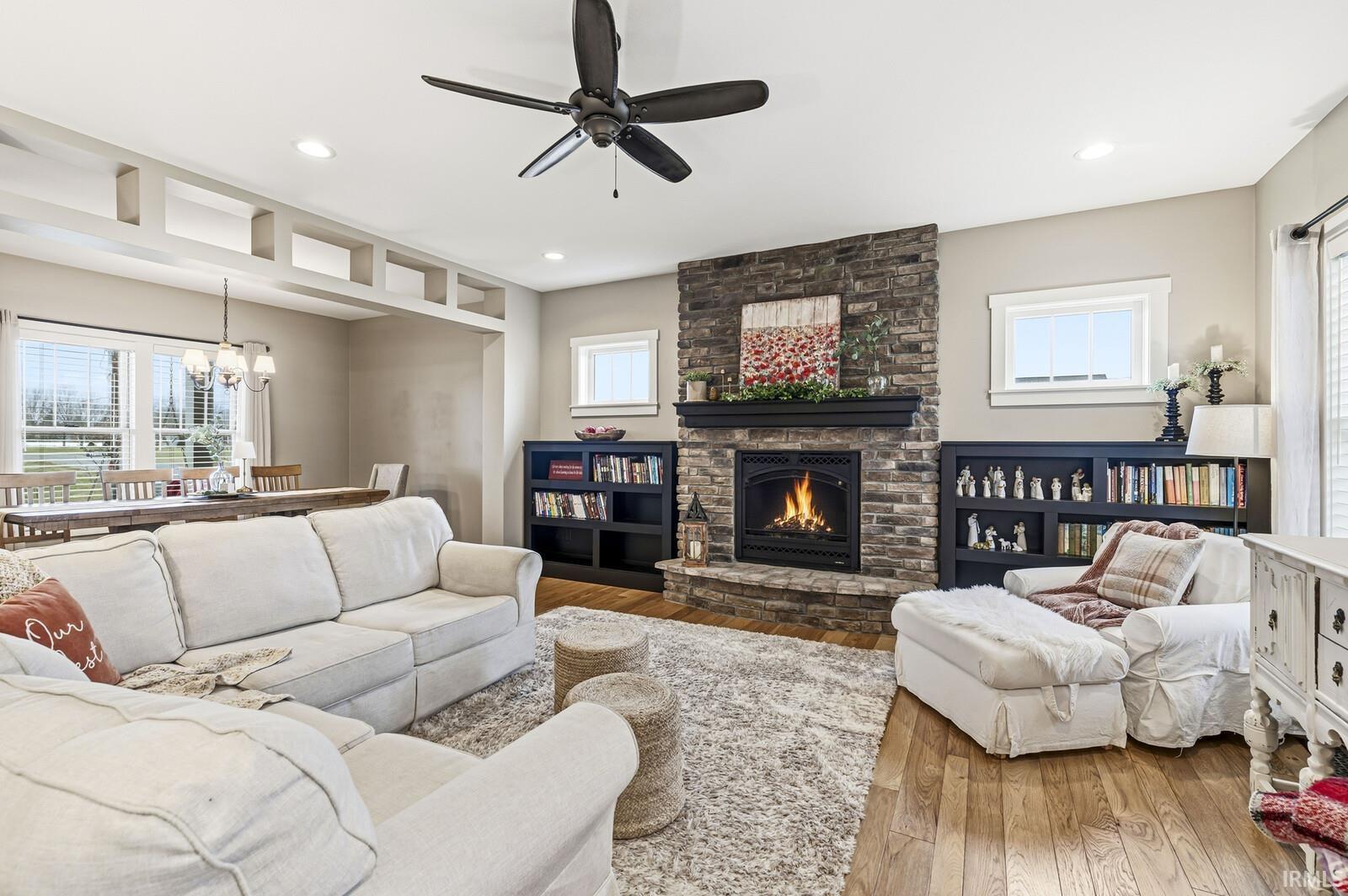 Living room featuring a fireplace, wood-type flooring, a chandelier, a ceiling fan, and recessed lighting