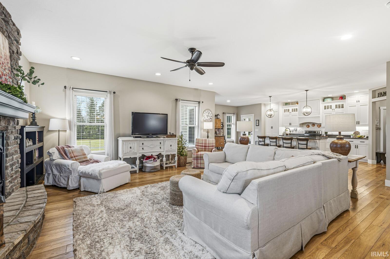 Living room with a fireplace, light wood-type flooring, ceiling fan, and recessed lighting