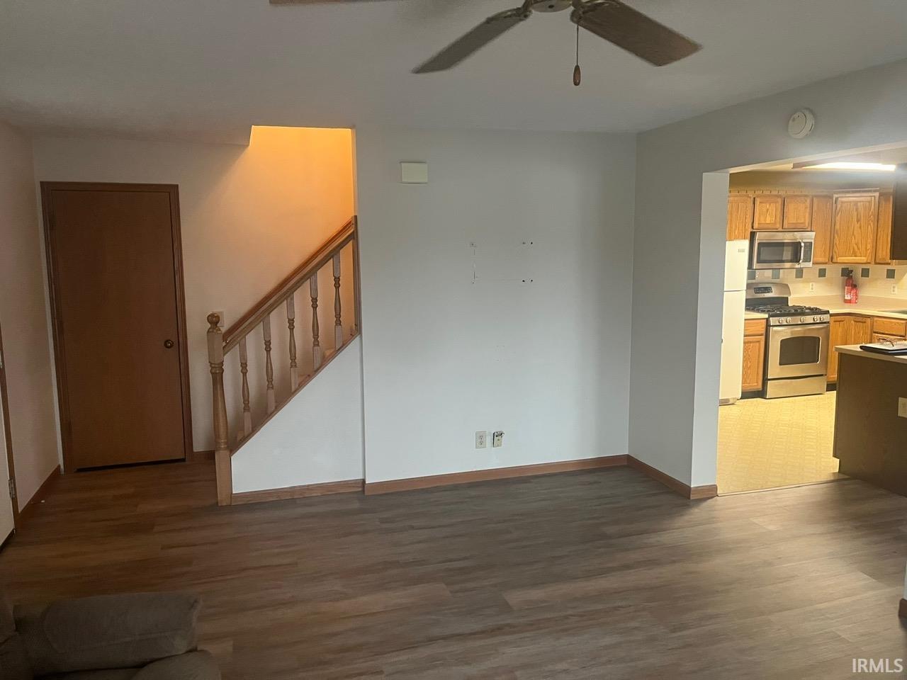 Unfurnished living room featuring dark wood finished floors, ceiling fan, and stairs