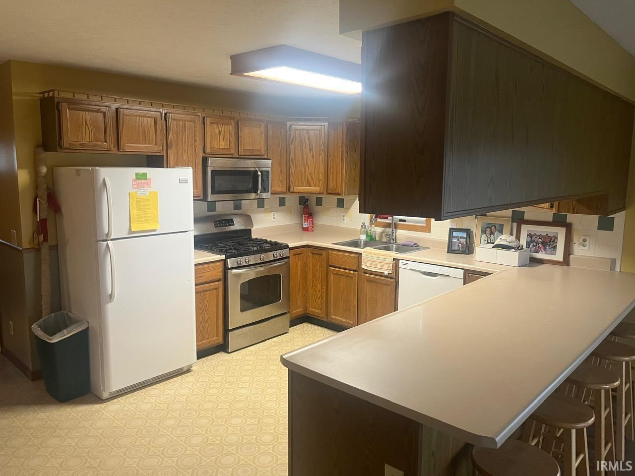 Kitchen featuring light flooring, a kitchen breakfast bar, appliances with stainless steel finishes, a peninsula, and brown cabinets
