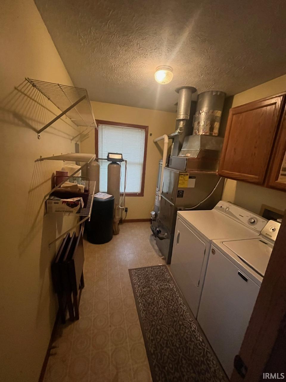 Laundry room featuring cabinet space, washer and clothes dryer, a textured ceiling, heating unit, and light flooring