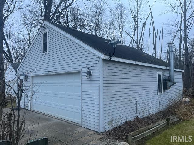 View of side of property featuring a garage and a shingled roof