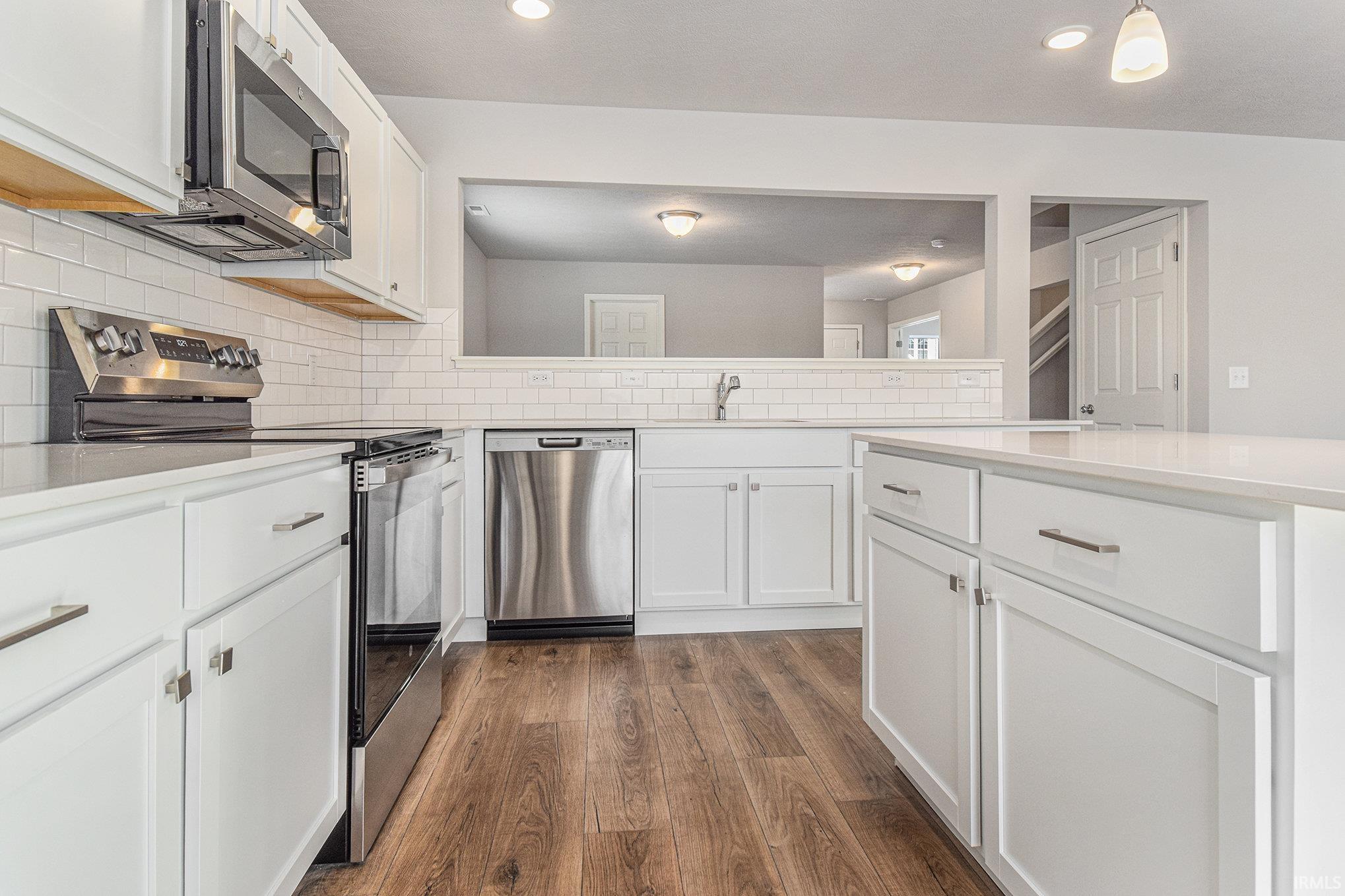The kitchen includes a center island for additional storage and prep space.  The extended edge can fit barstools and there is pendant lighting above. Quartz counters are accented by subway tile backsplash and select stainless steel appliances included.