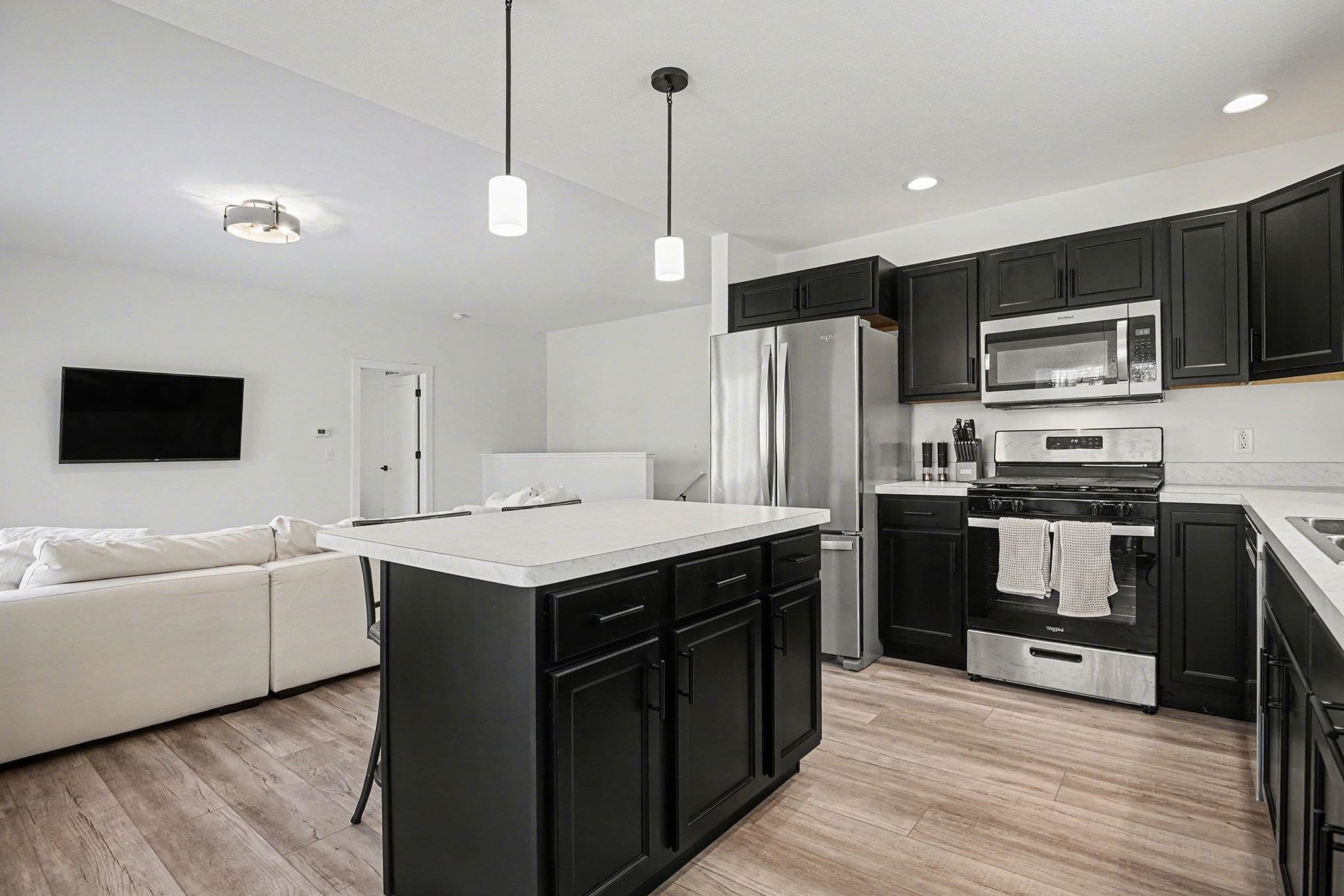 Kitchen featuring dark cabinetry, appliances with stainless steel finishes, open floor plan, hanging light fixtures, and recessed lighting
