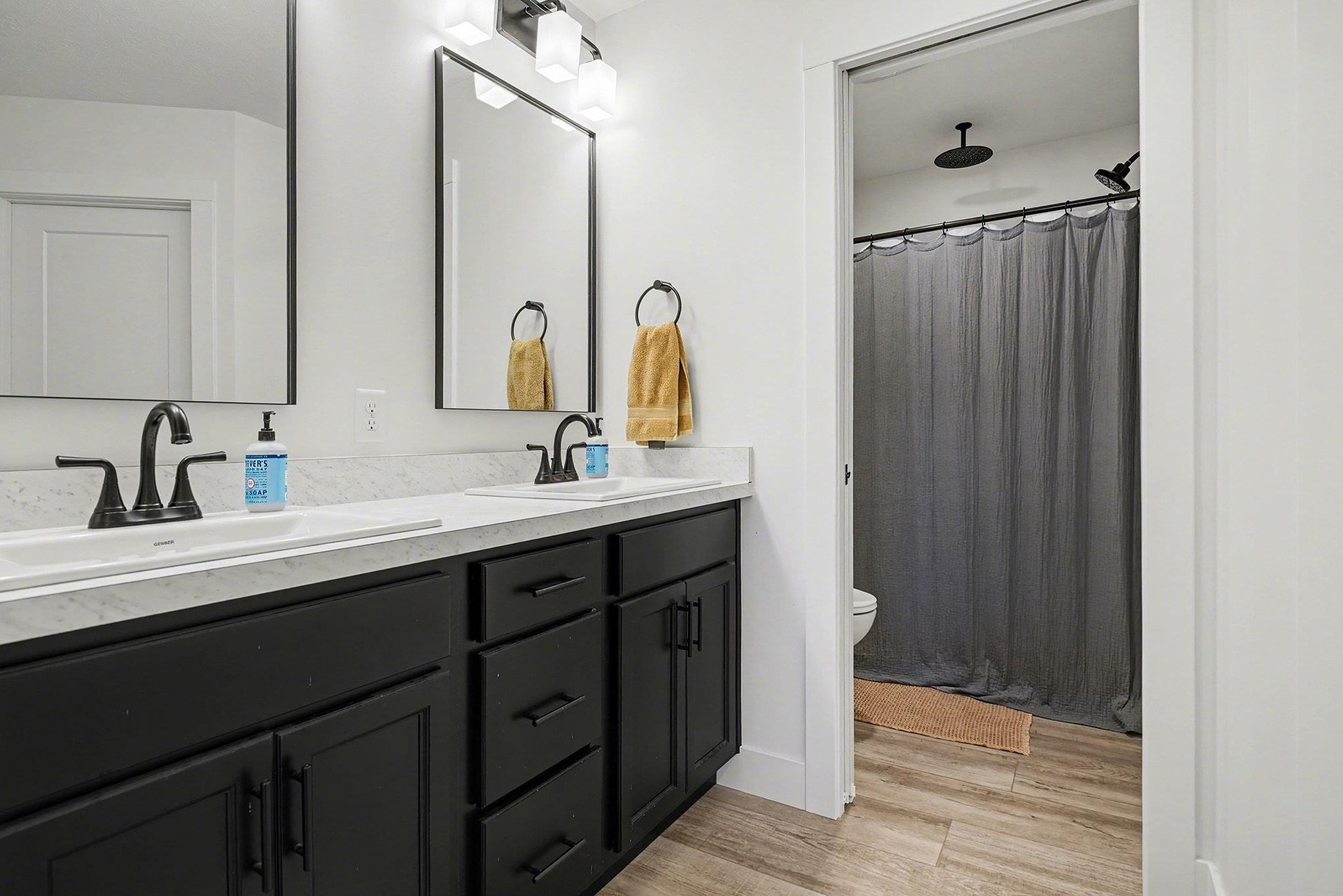 Full bath featuring a shower with shower curtain, double vanity, and light wood-style flooring