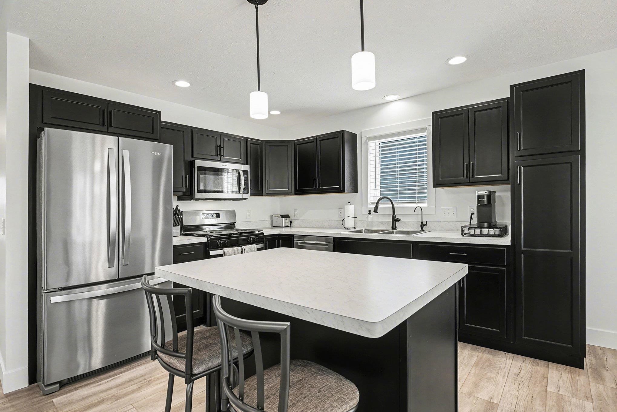 Kitchen with dark cabinetry, appliances with stainless steel finishes, a kitchen breakfast bar, hanging light fixtures, and light countertops