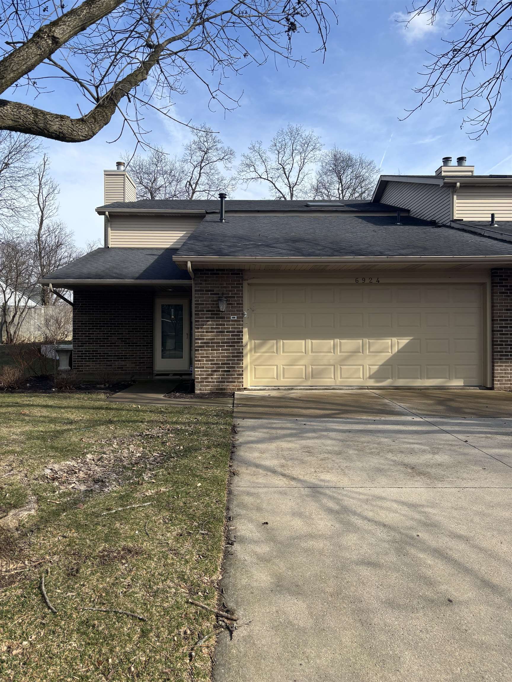 Mid-century home featuring a chimney, concrete driveway, a garage, roof with shingles, and brick siding