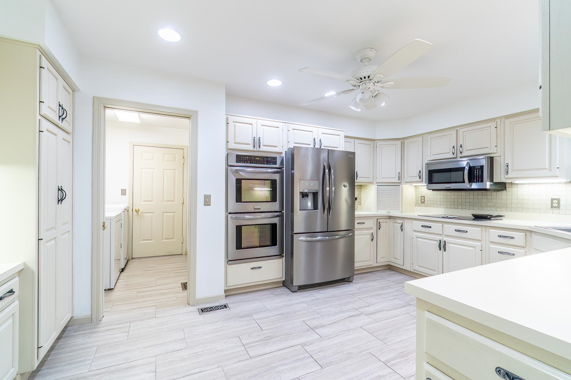 Kitchen with light countertops, appliances with stainless steel finishes, ceiling fan, tasteful backsplash, and washer and clothes dryer
