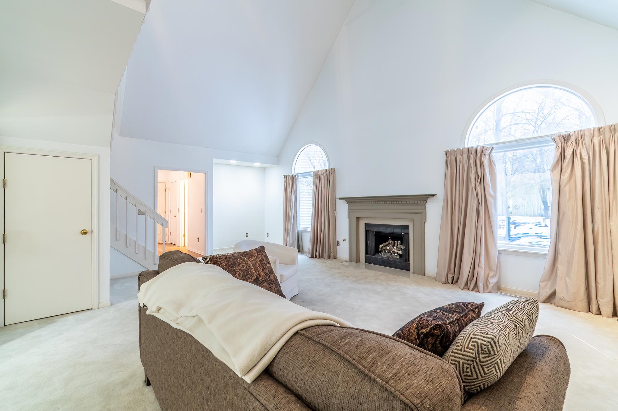 Carpeted living area featuring high vaulted ceiling, a fireplace, and stairway