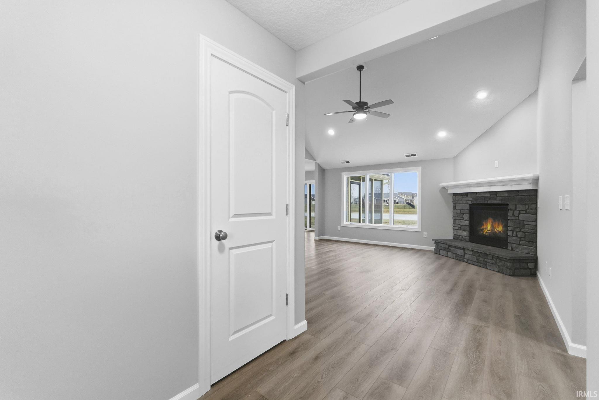 Unfurnished living room featuring a fireplace, light wood-type flooring, a ceiling fan, lofted ceiling, and a textured ceiling