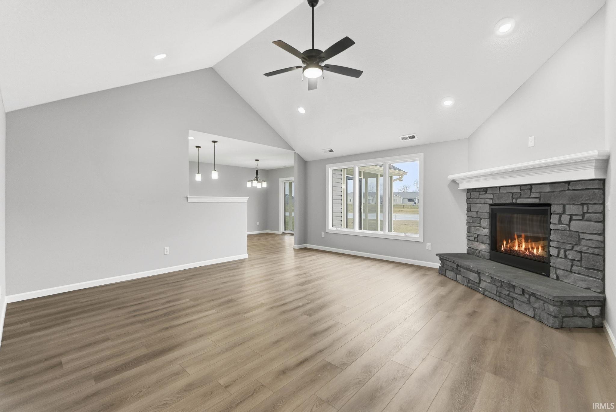 Unfurnished living room with a stone fireplace, wood finished floors, ceiling fan, a chandelier, and high vaulted ceiling