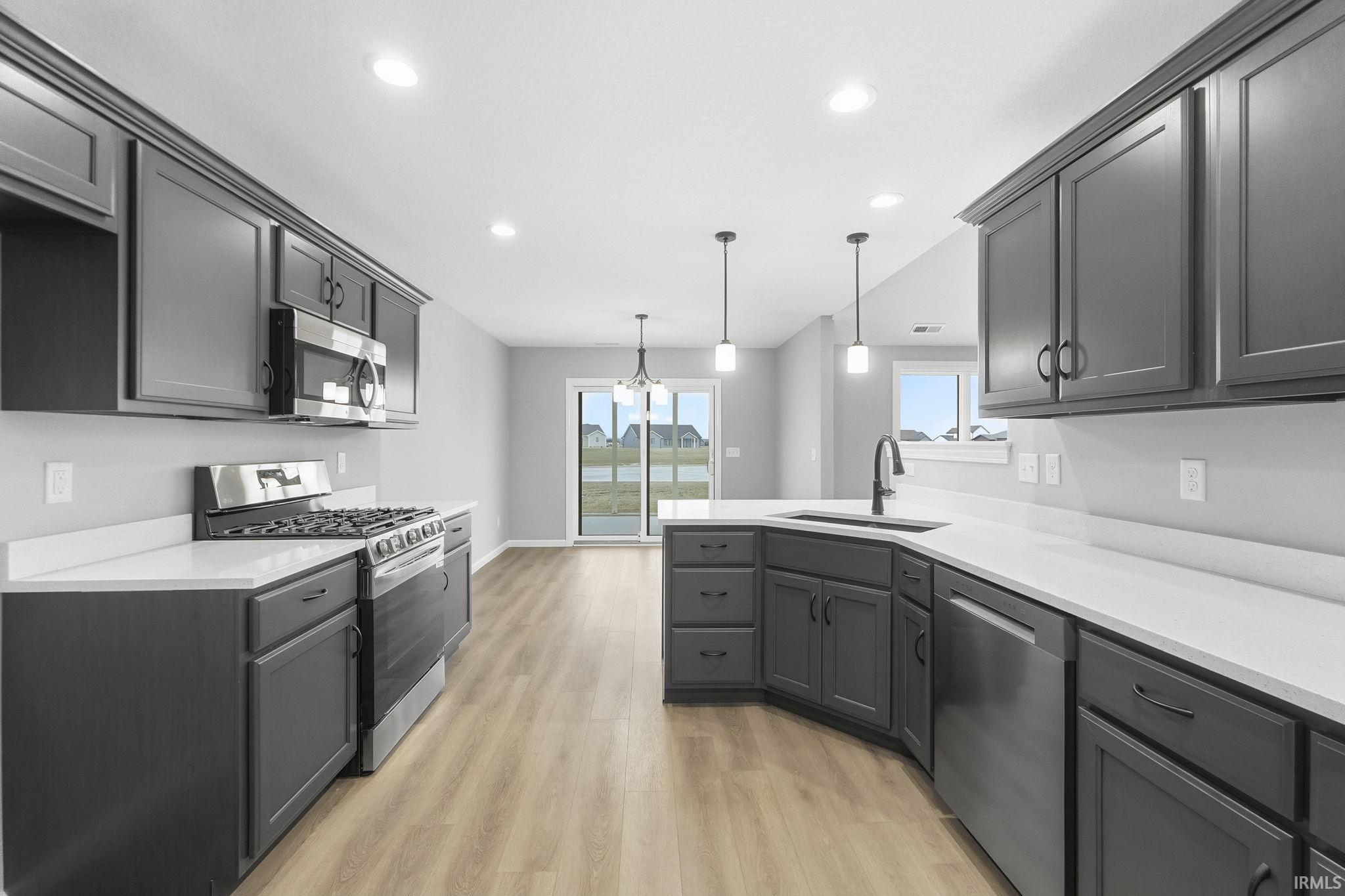 Kitchen featuring appliances with stainless steel finishes, pendant lighting, a peninsula, light wood-style flooring, and a chandelier
