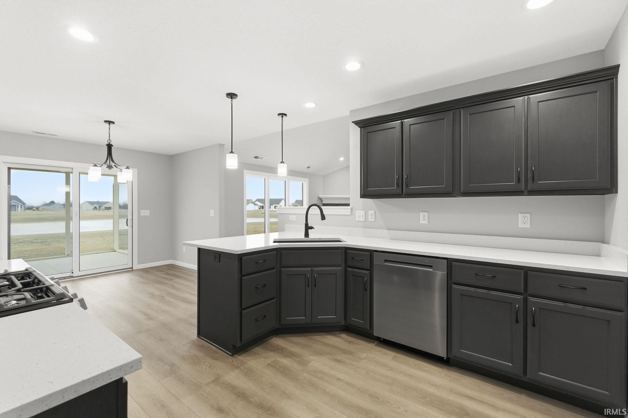 Kitchen featuring a peninsula, stainless steel dishwasher, decorative light fixtures, light wood-type flooring, and vaulted ceiling