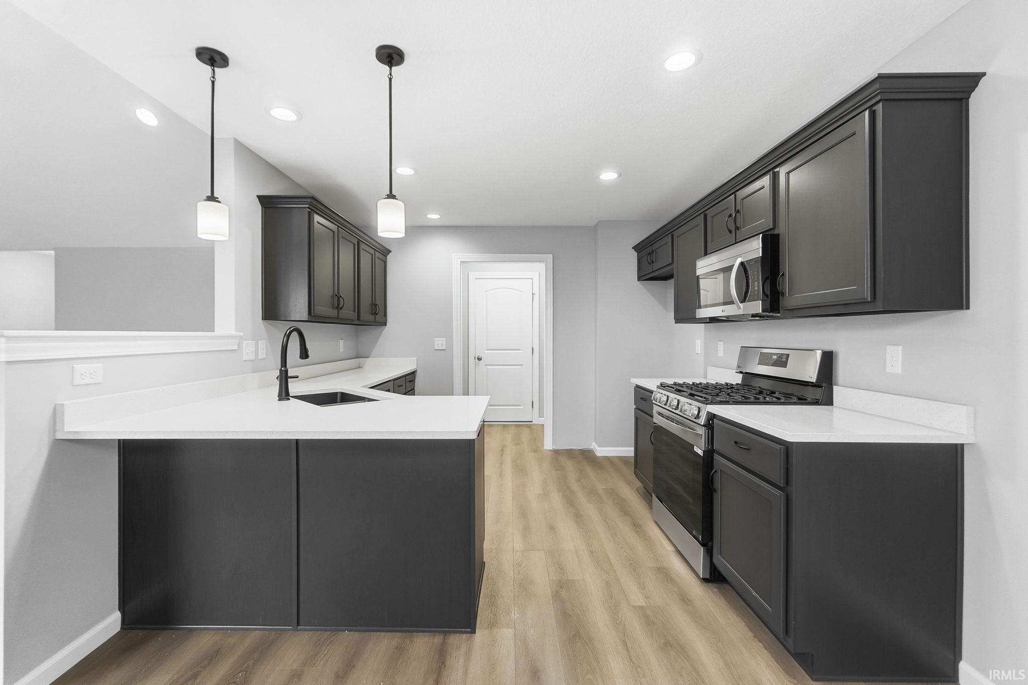 Kitchen with stainless steel appliances, a peninsula, light wood-style floors, hanging light fixtures, and light stone countertops