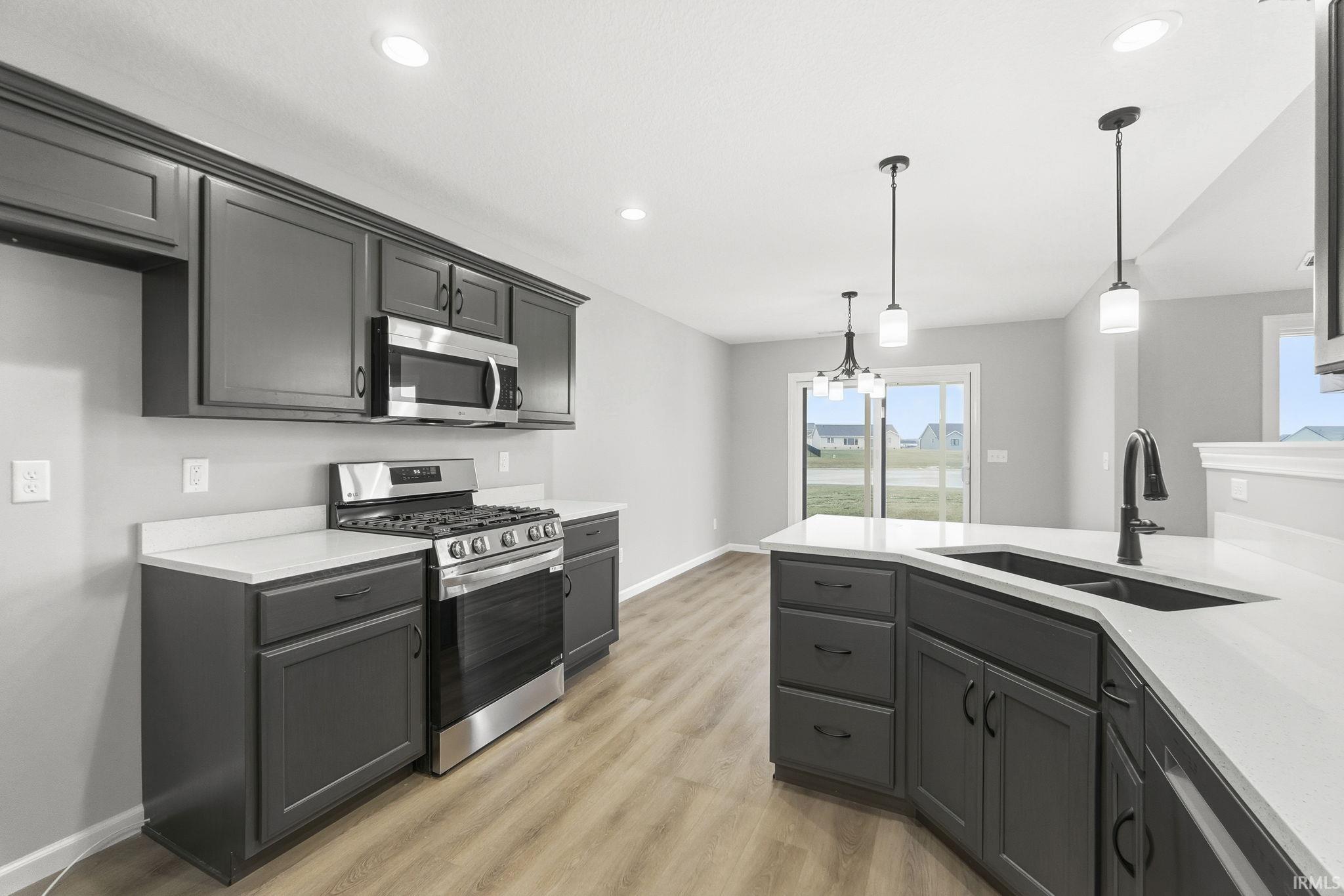 Kitchen featuring stainless steel appliances, hanging light fixtures, light stone counters, light wood-style flooring, and recessed lighting