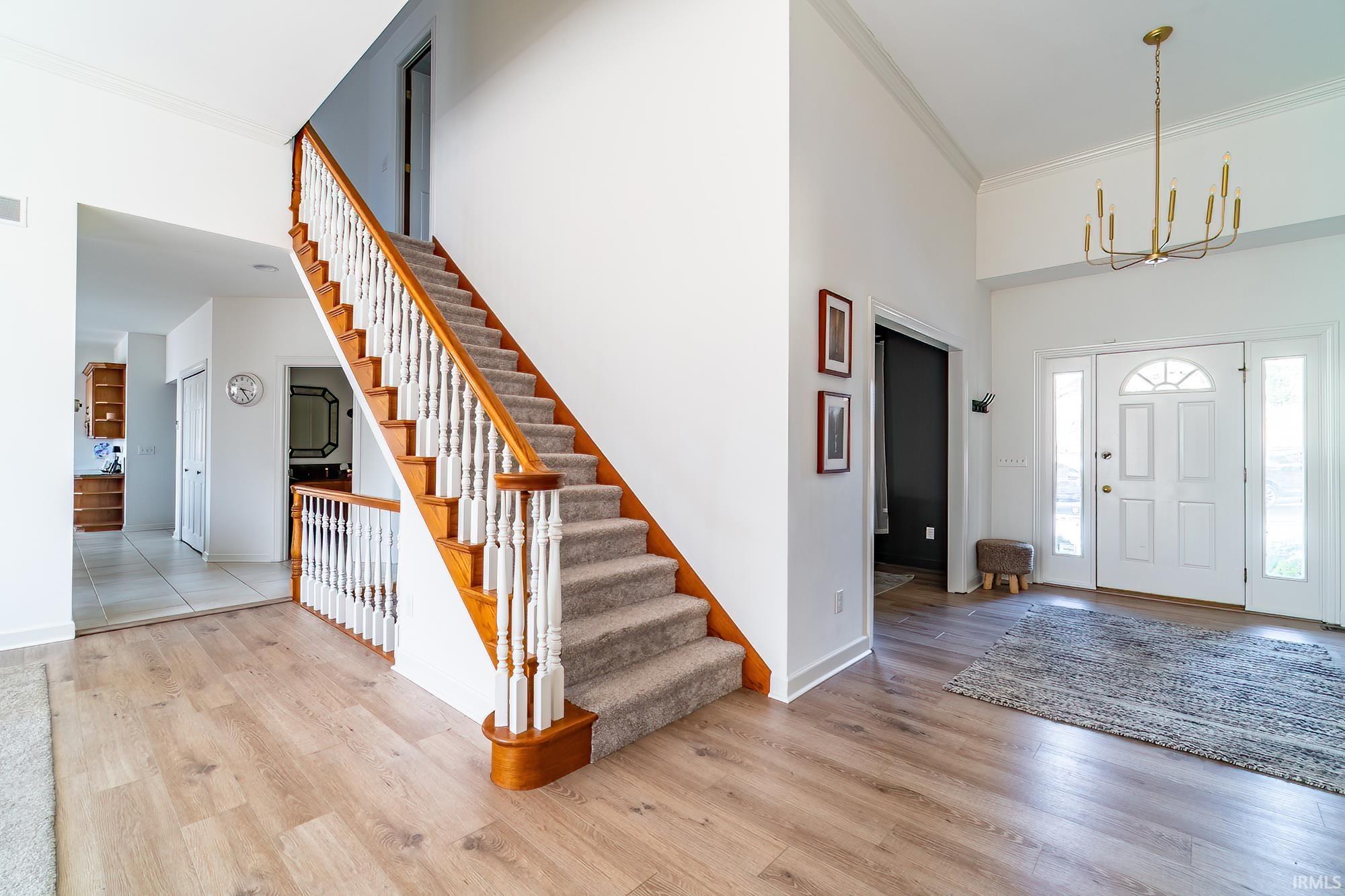 Entryway with ornamental molding, light wood-style flooring, stairway, a towering ceiling, and a chandelier
