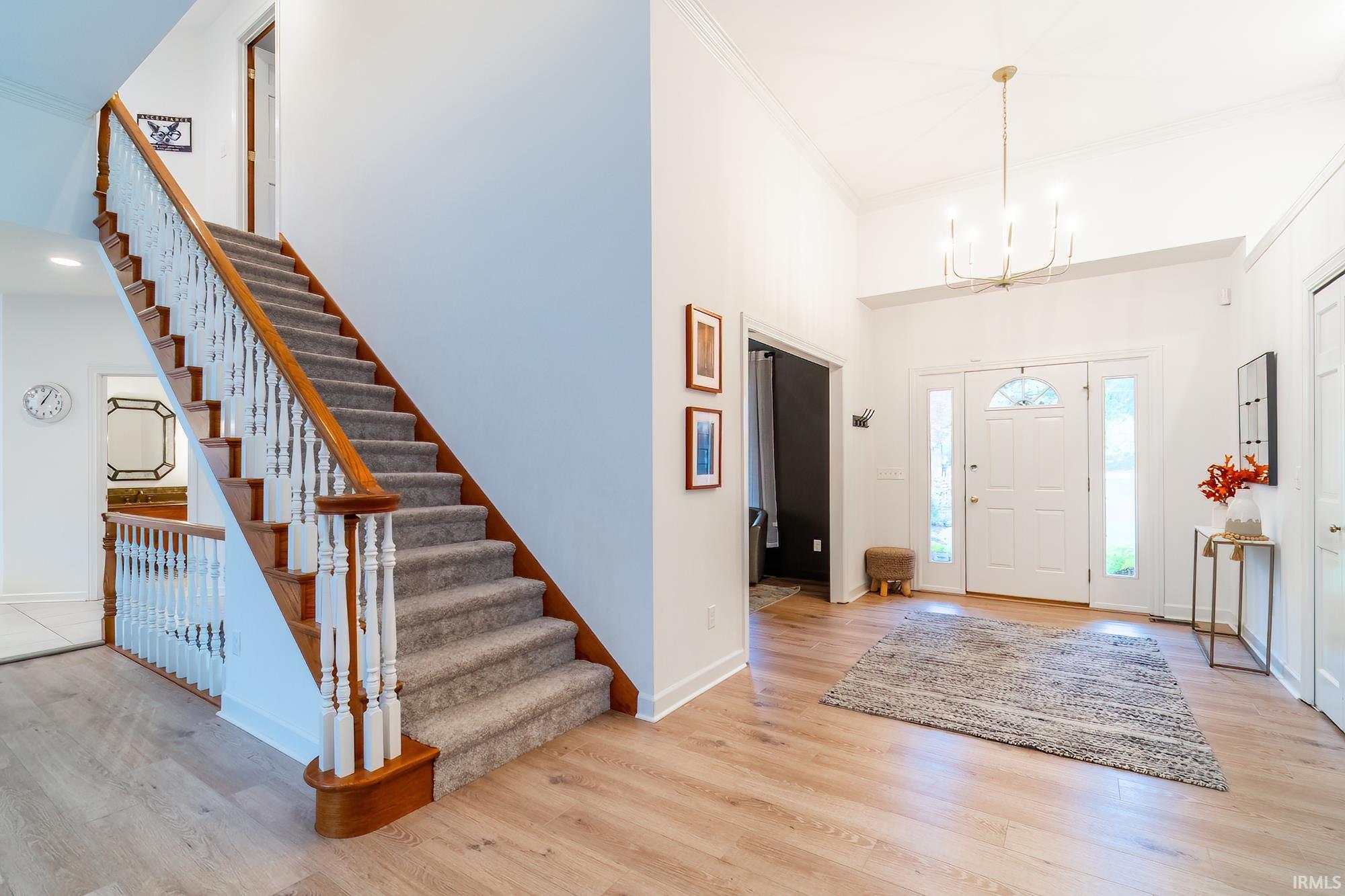 Foyer featuring light wood-style flooring, crown molding, stairway, a chandelier, and a high ceiling