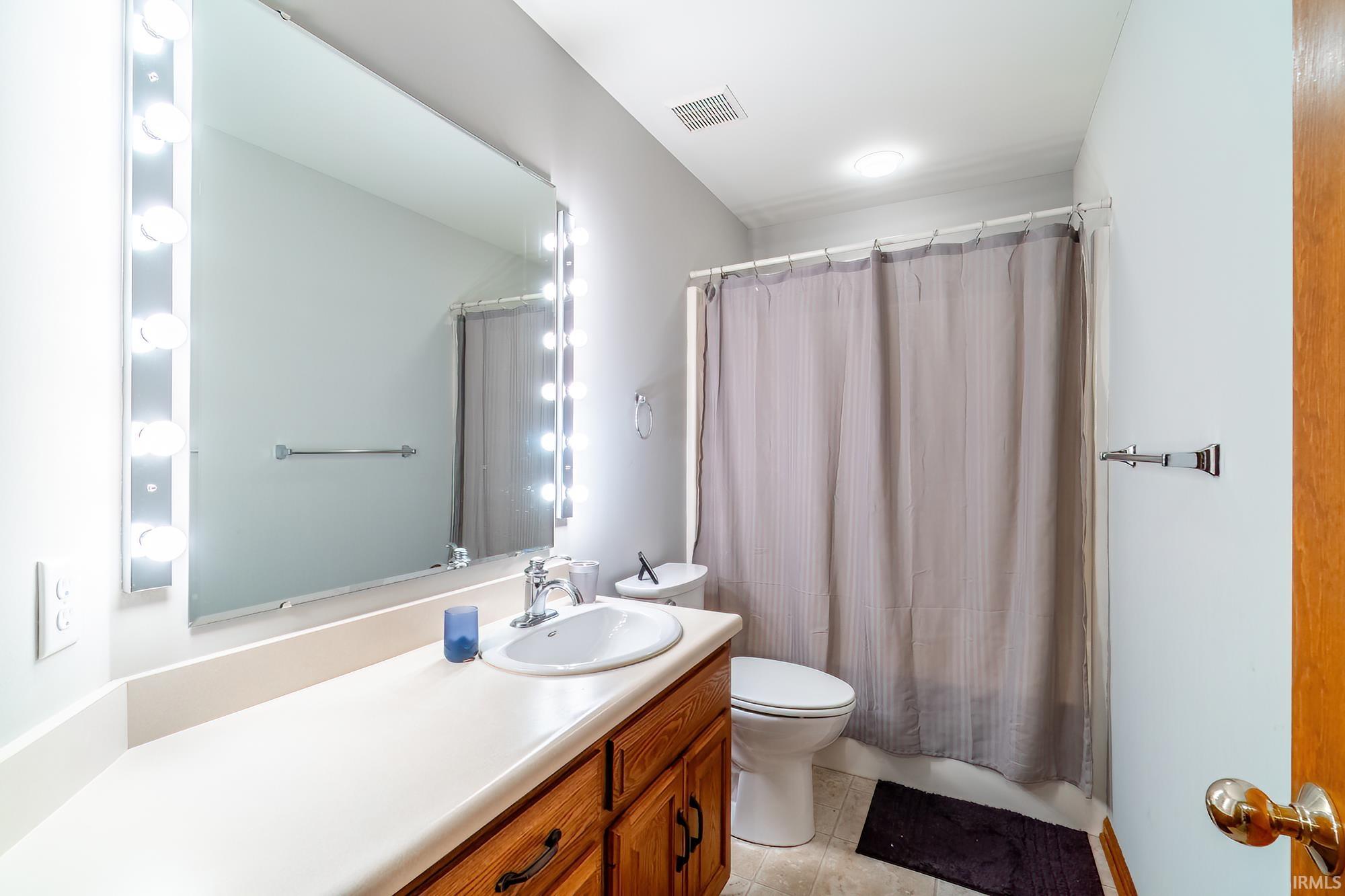 Full bathroom with vanity, shower / bathtub combination with curtain, and light tile patterned floors