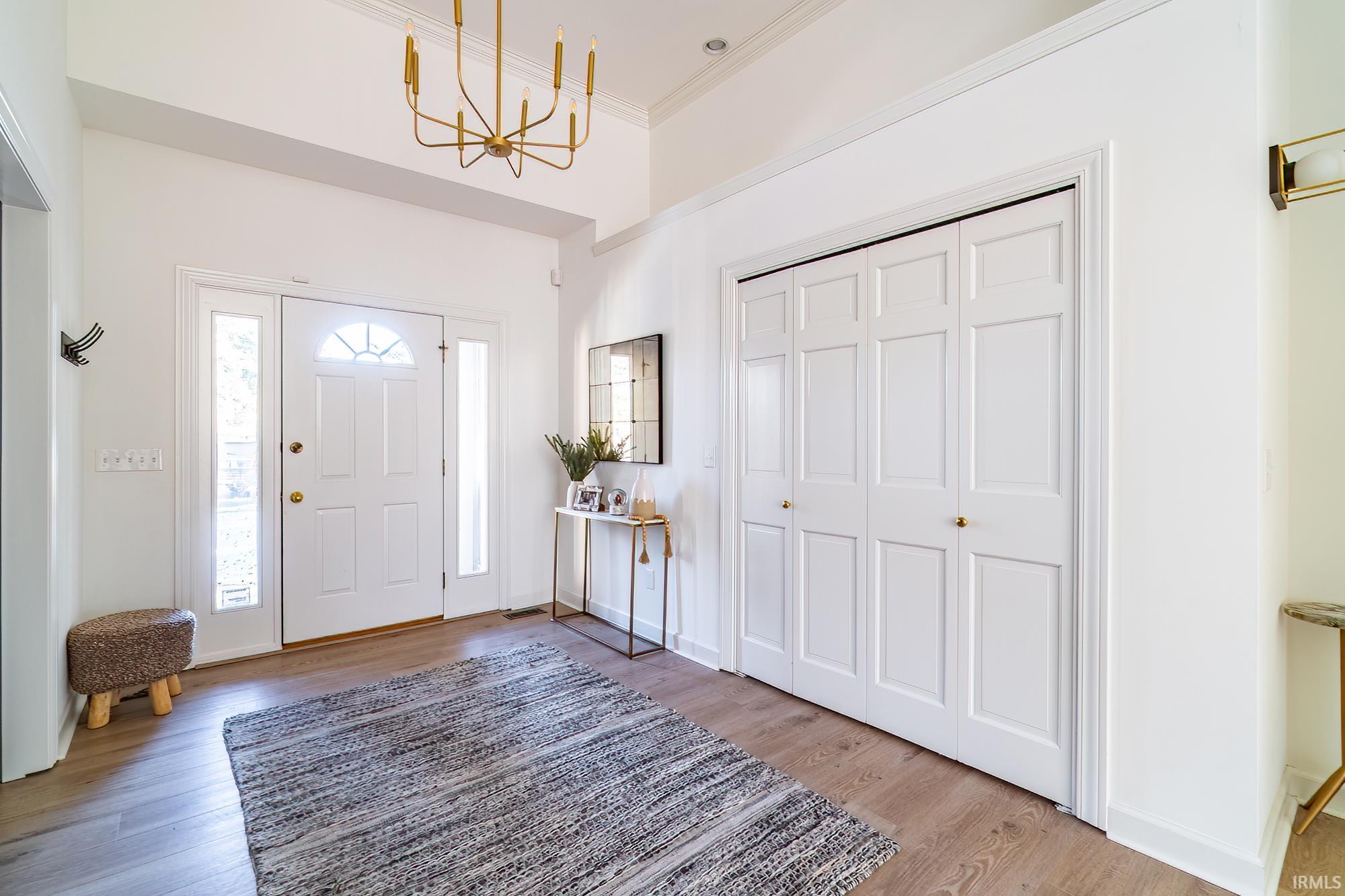 Entryway with light wood-type flooring, ornamental molding, and a chandelier