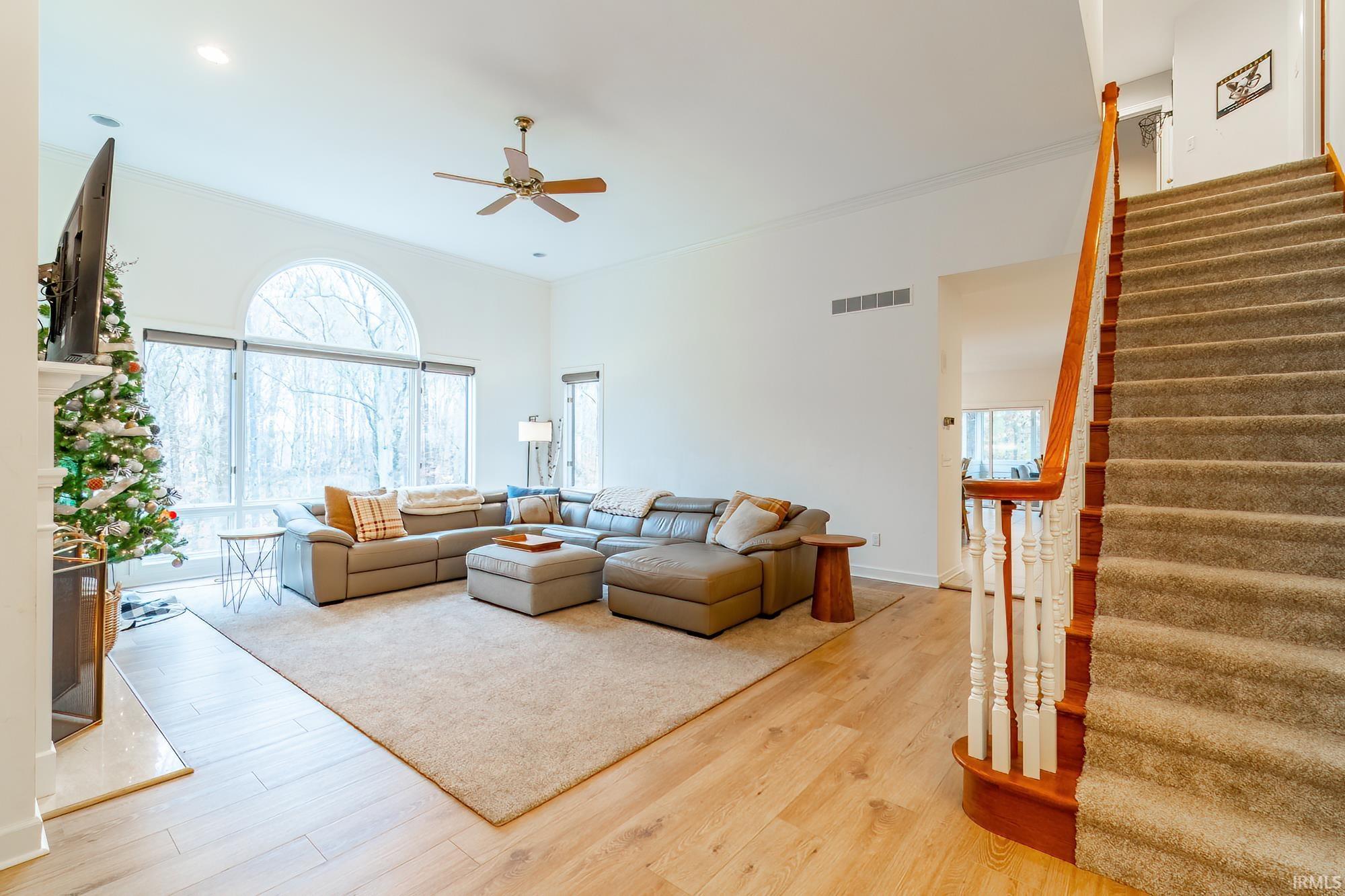 Living room featuring stairs, wood finished floors, healthy amount of natural light, ornamental molding, and ceiling fan