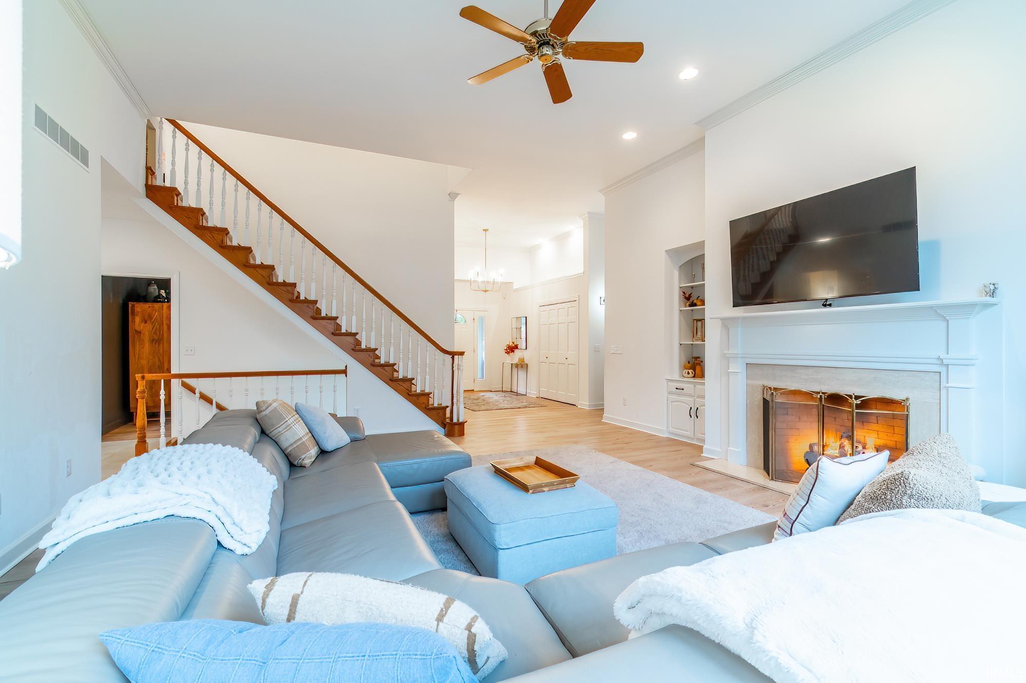 Living room featuring crown molding, built in shelves, a premium fireplace, wood finished floors, and a ceiling fan