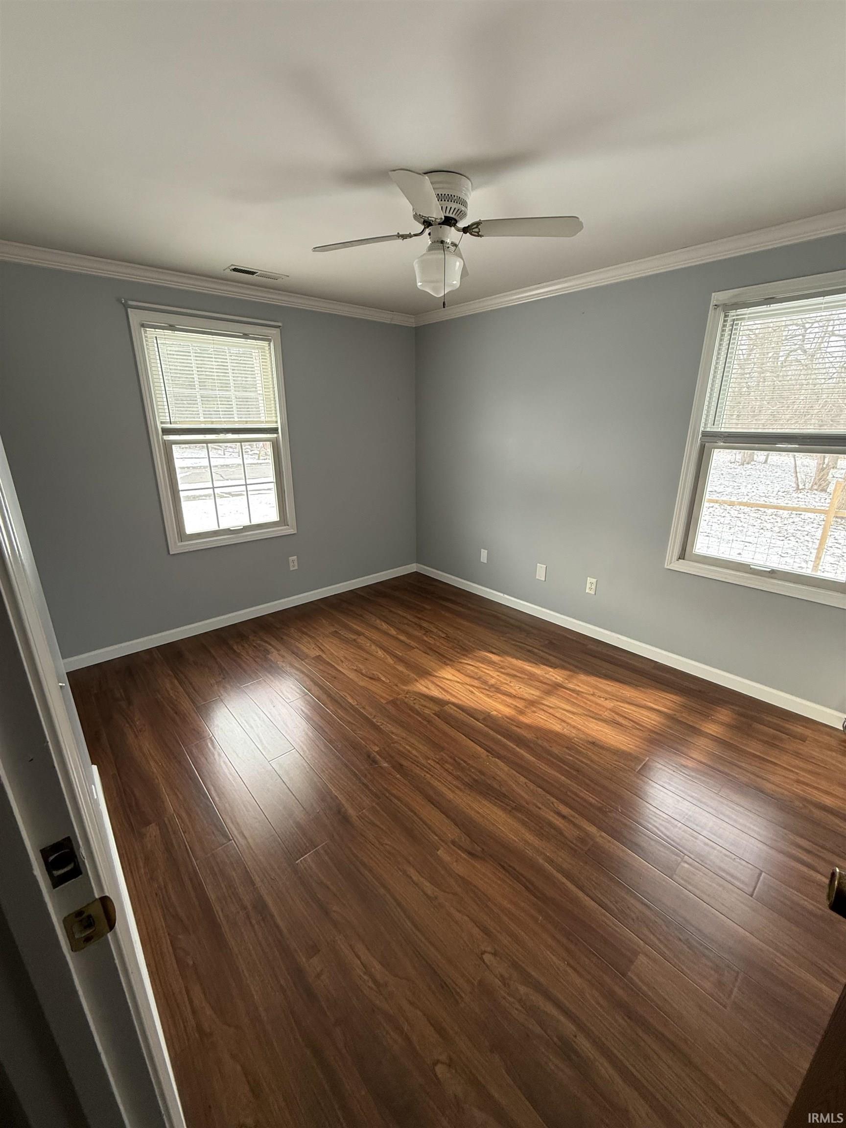 Empty room with plenty of natural light, wood finished floors, ornamental molding, and a ceiling fan