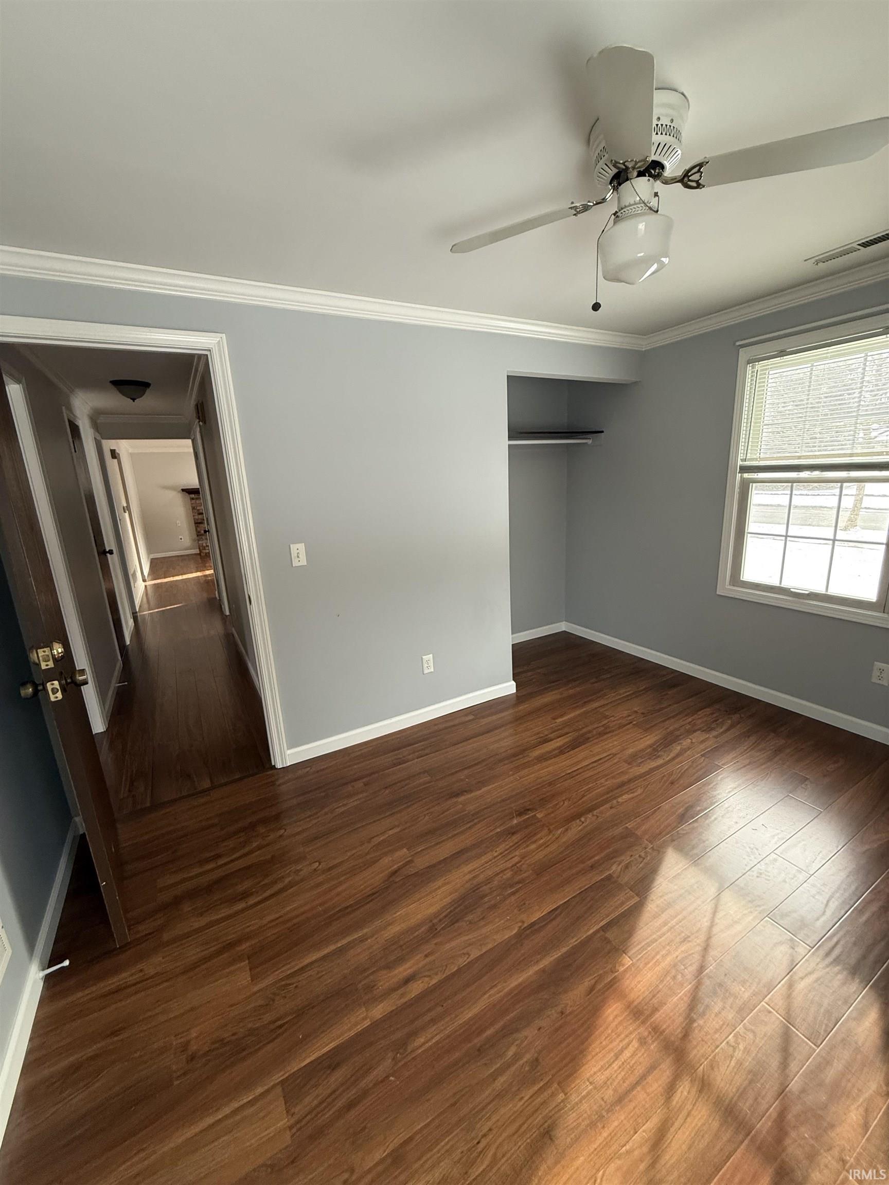Unfurnished bedroom with dark wood-type flooring, ceiling fan, and ornamental molding