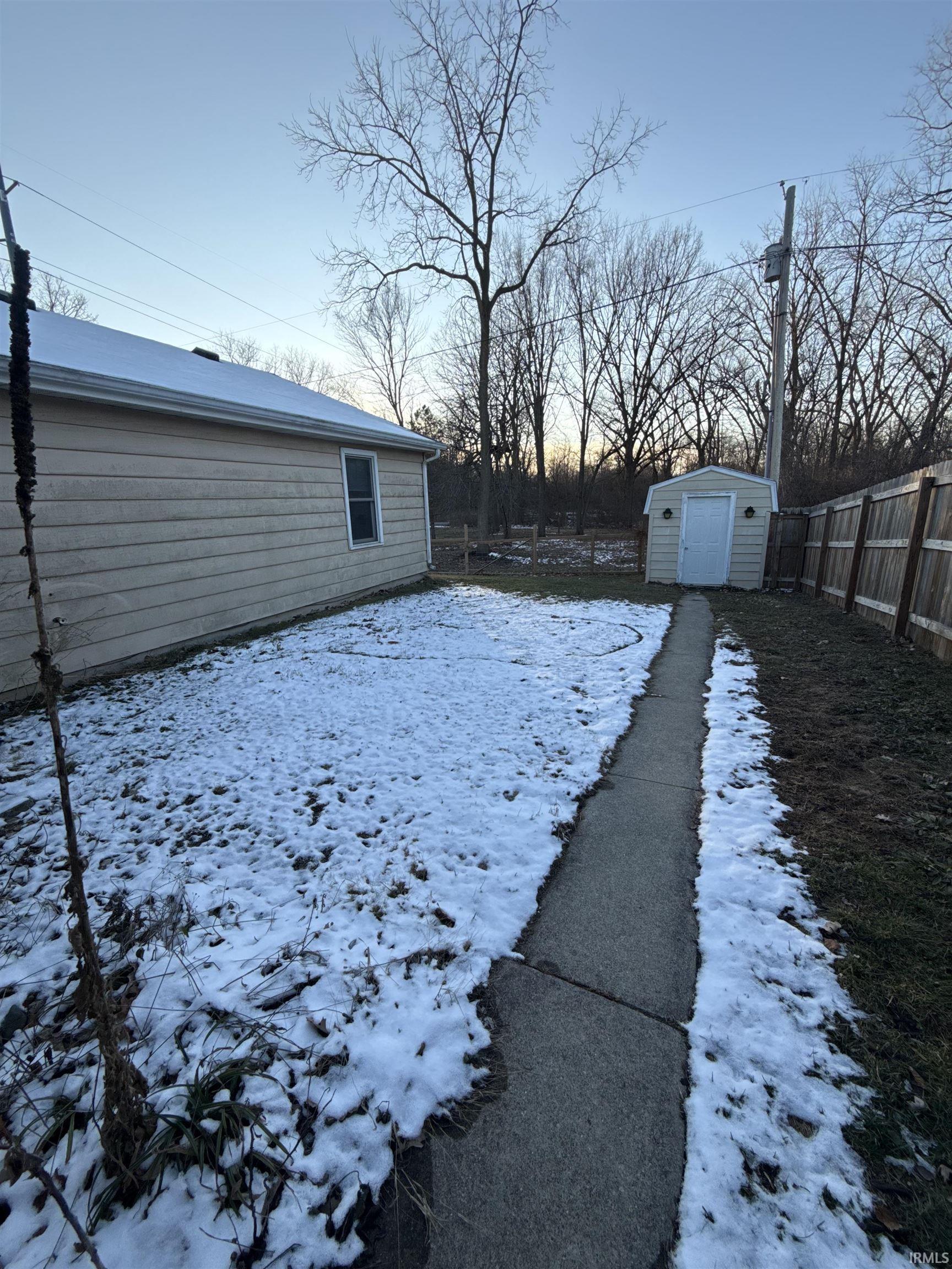 Snowy yard featuring a fenced backyard and a shed