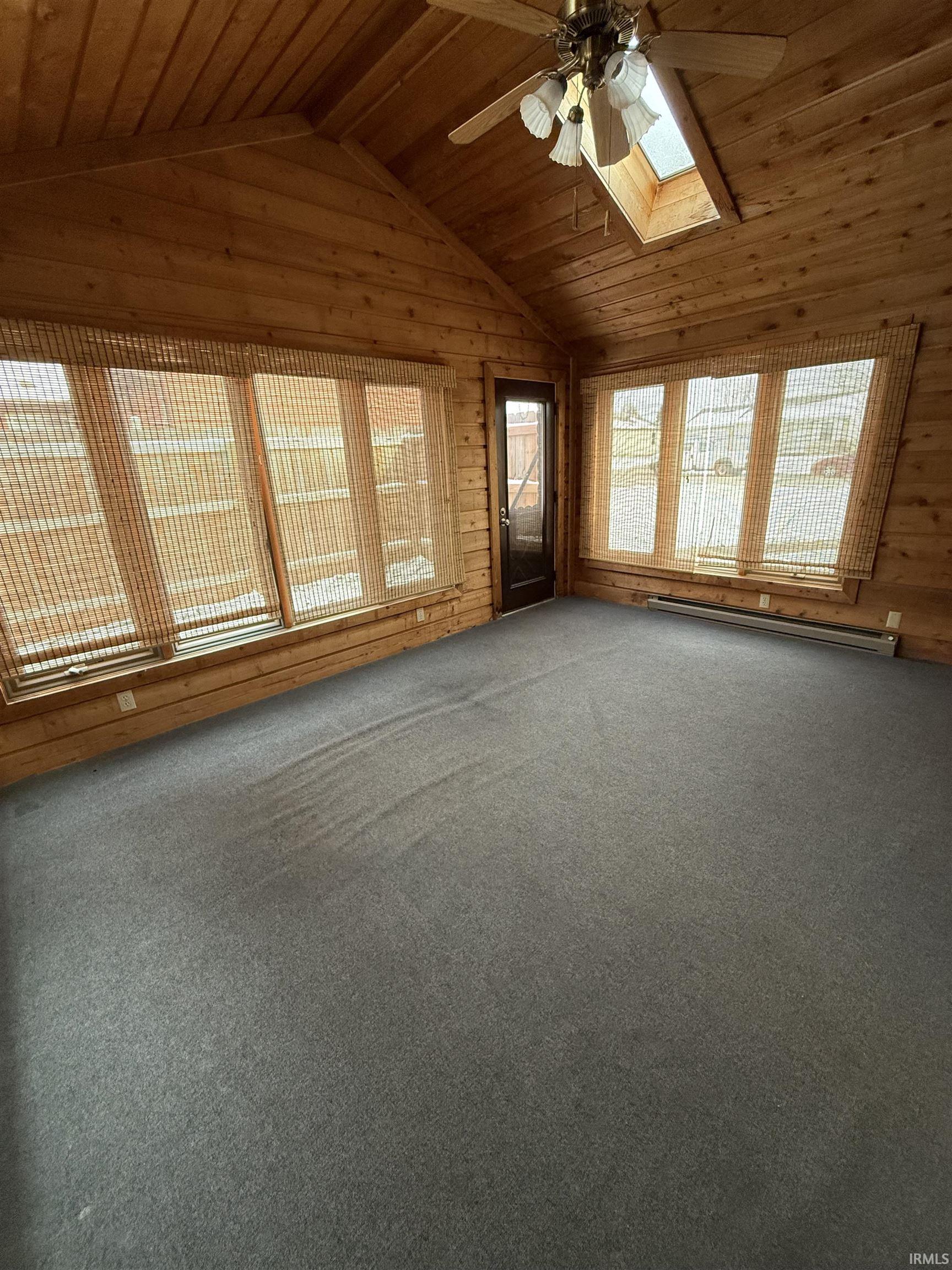 Unfurnished living room with lofted ceiling, a ceiling fan, wood ceiling, carpet floors, and a skylight