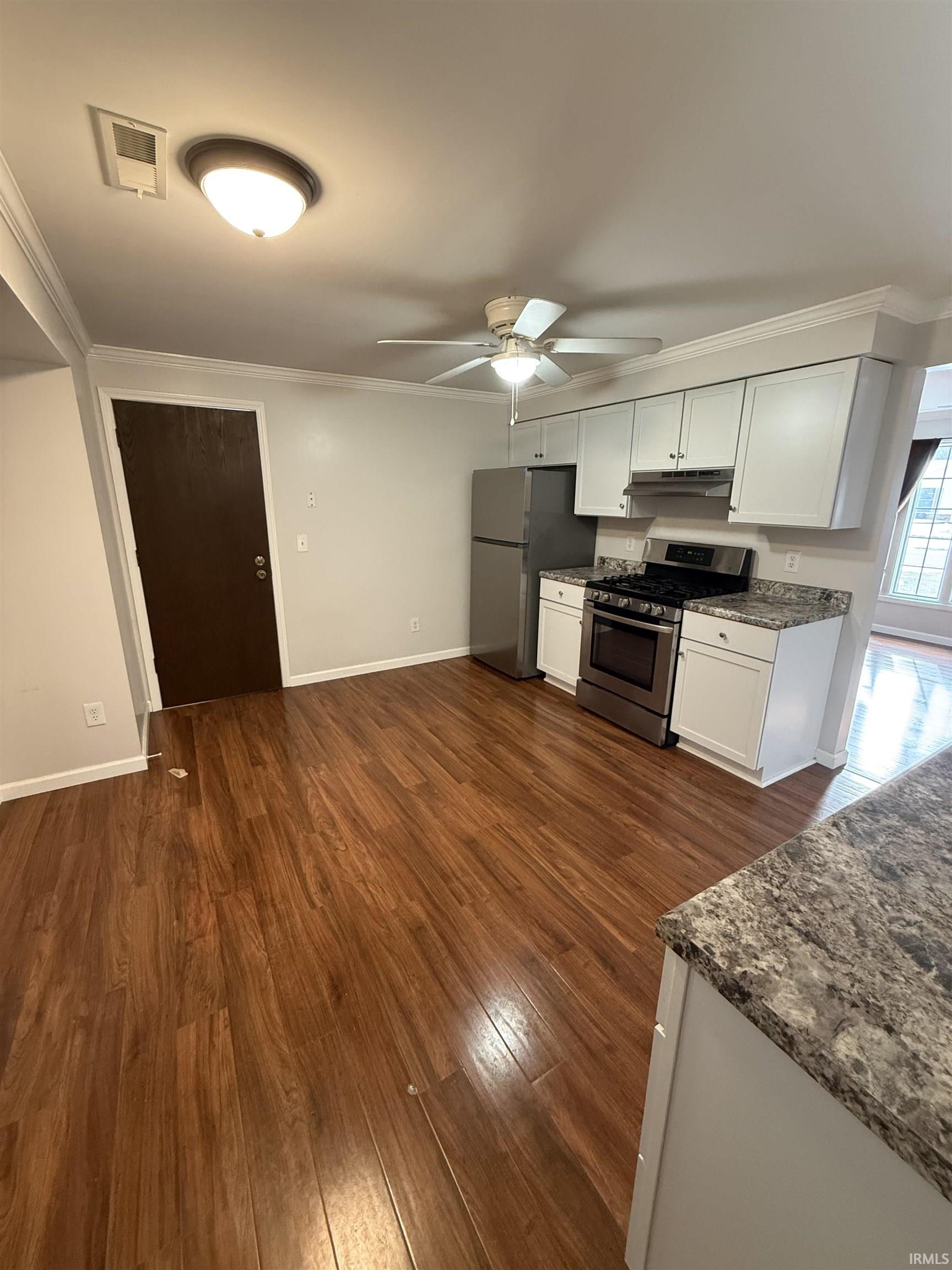 Kitchen featuring white cabinetry, appliances with stainless steel finishes, a ceiling fan, ornamental molding, and dark wood finished floors