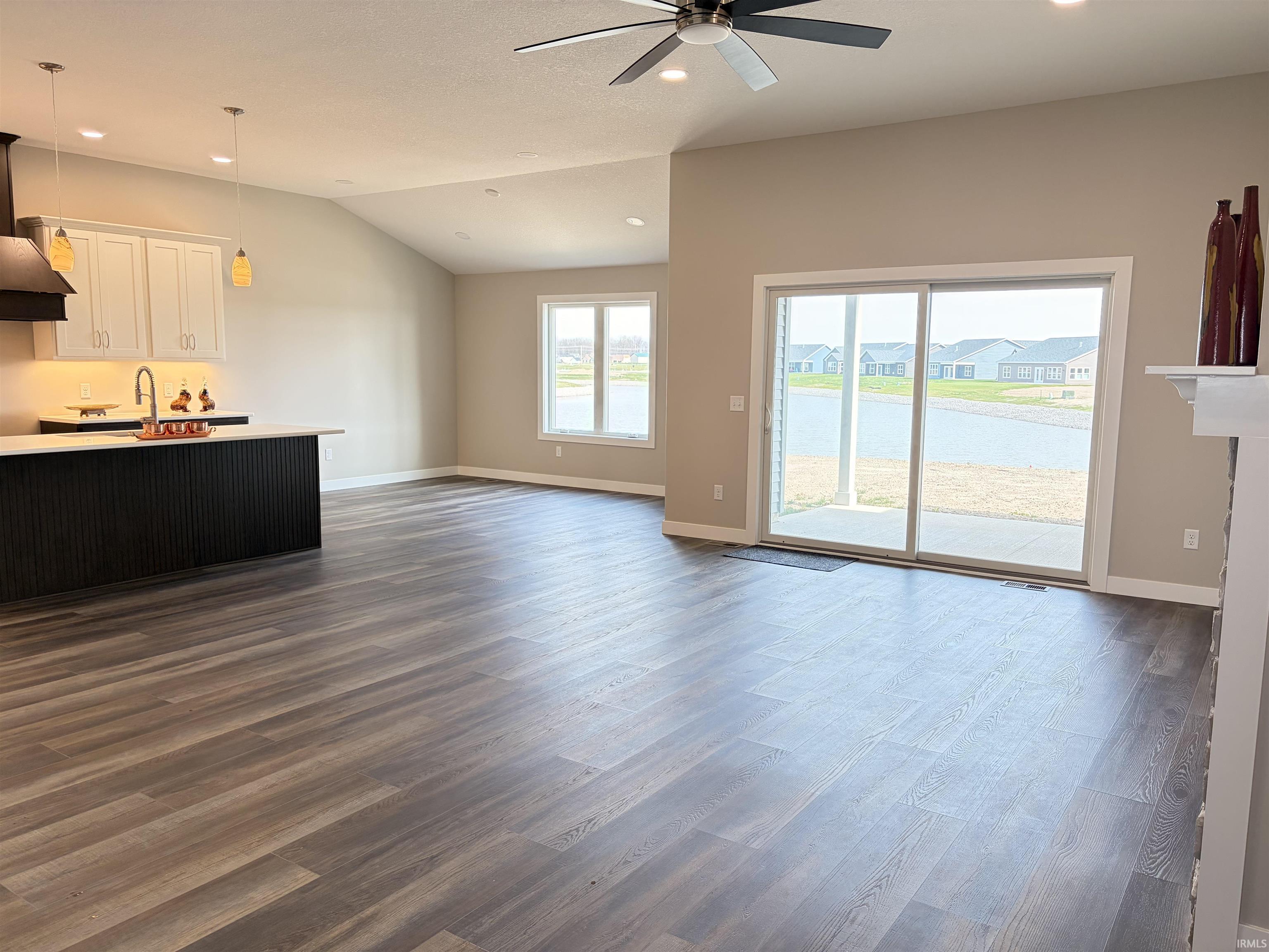 Unfurnished living room featuring recessed lighting, dark wood finished floors, a ceiling fan, lofted ceiling, and a water view