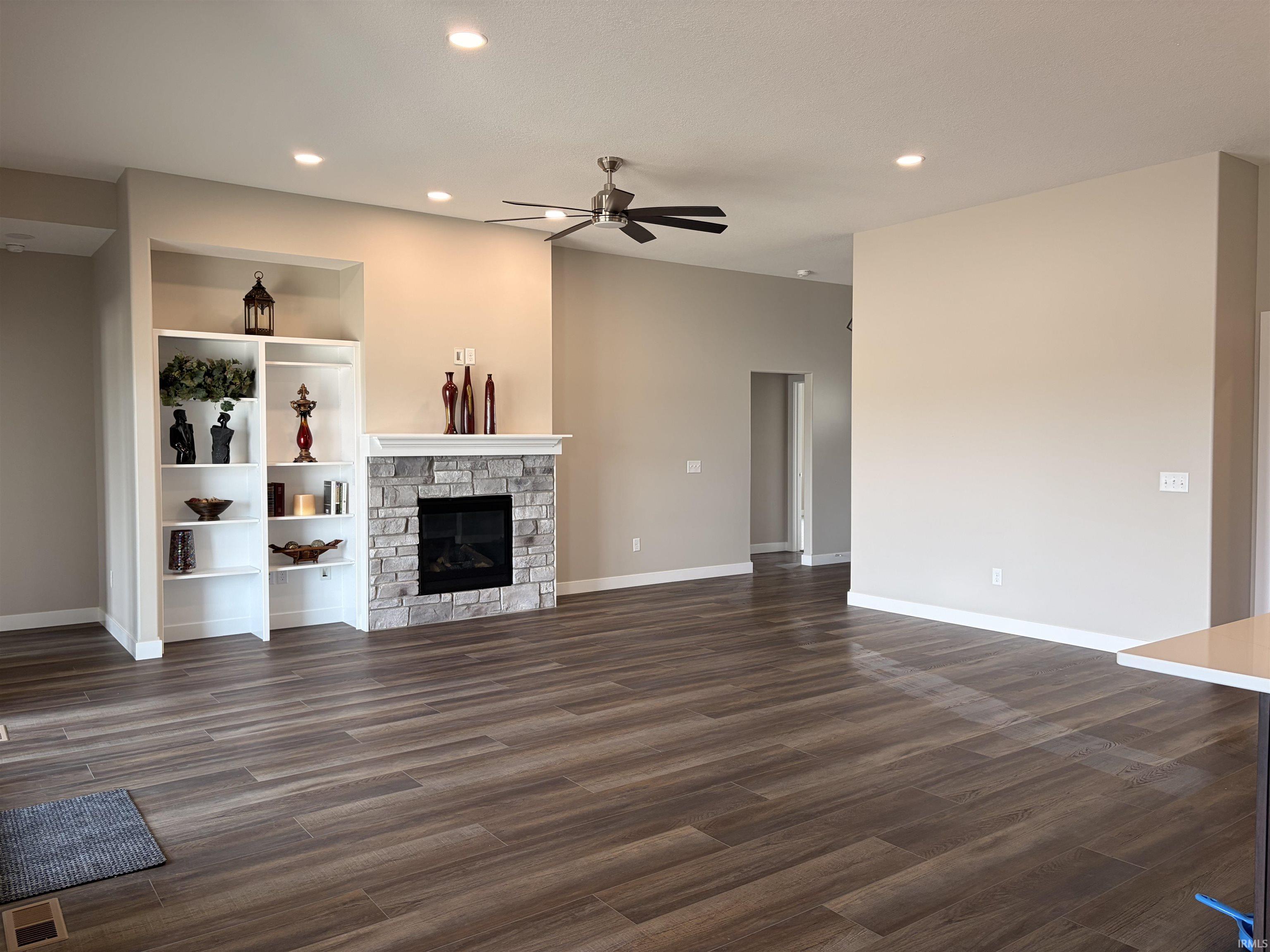 Unfurnished living room with a ceiling fan, recessed lighting, dark wood-style flooring, and a stone fireplace