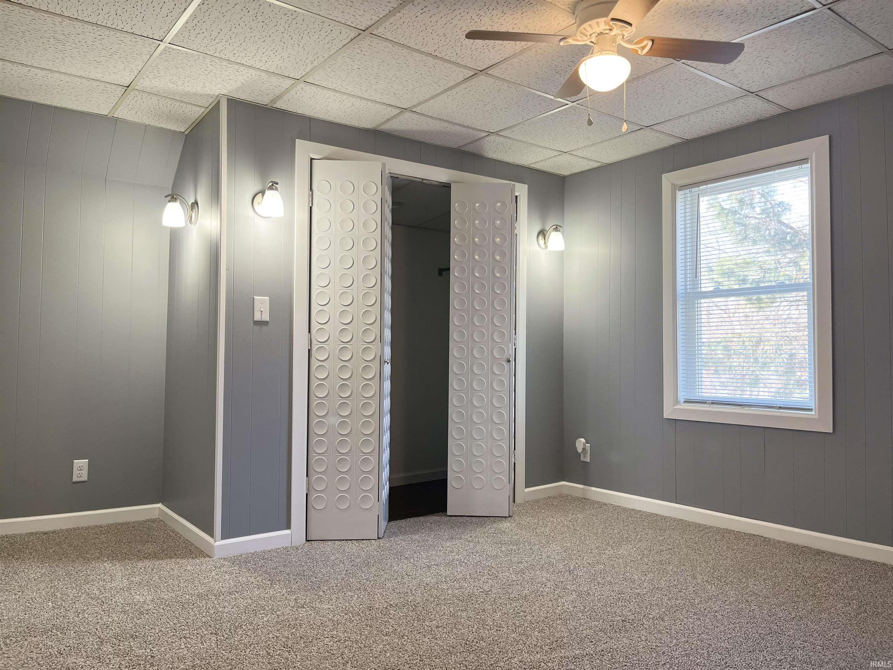 Unfurnished bedroom featuring a drop ceiling, carpet, wood walls, and ceiling fan