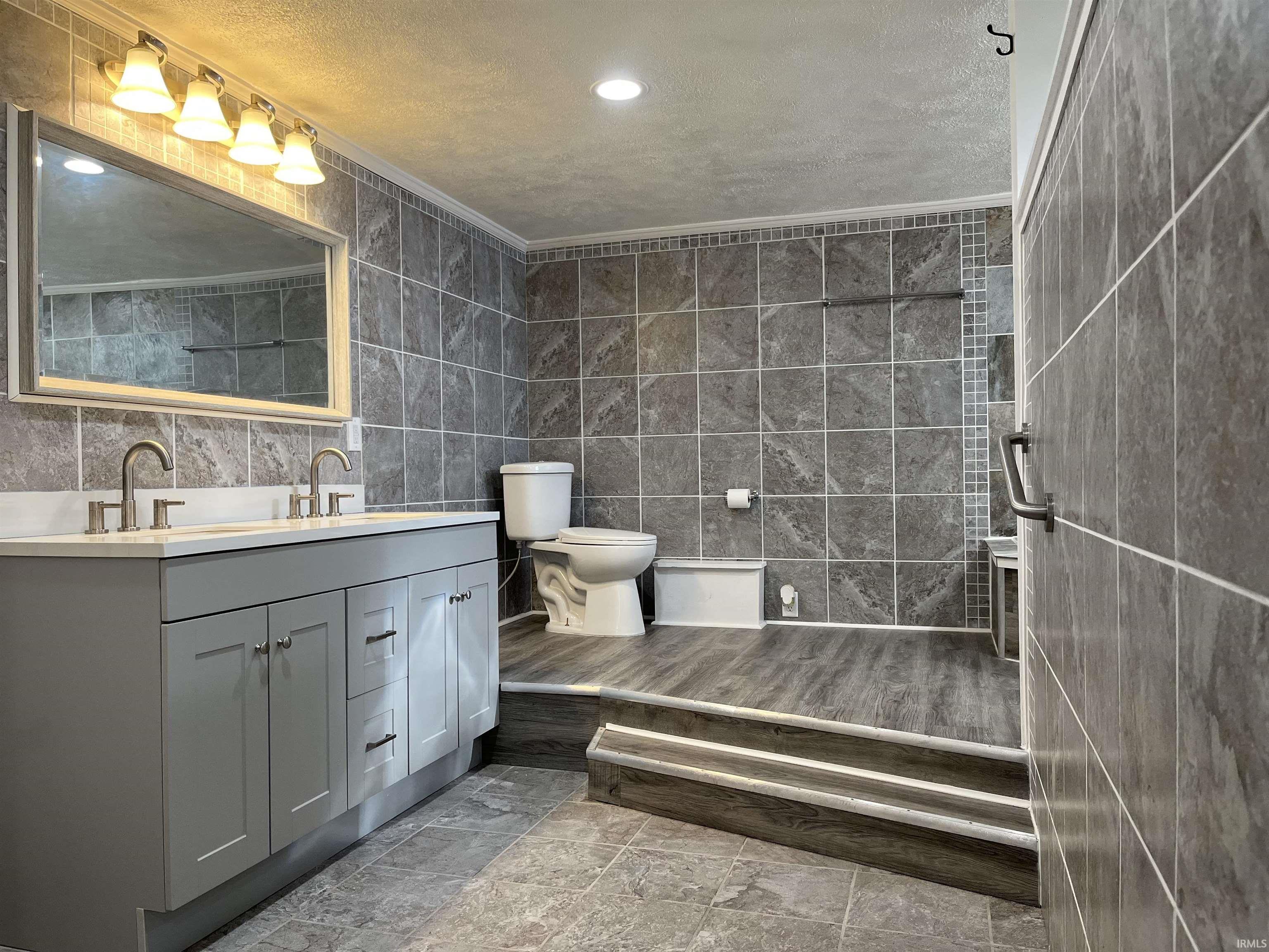 Lower Level Bathroom featuring tile walls, double vanity, recessed lighting, and crown molding