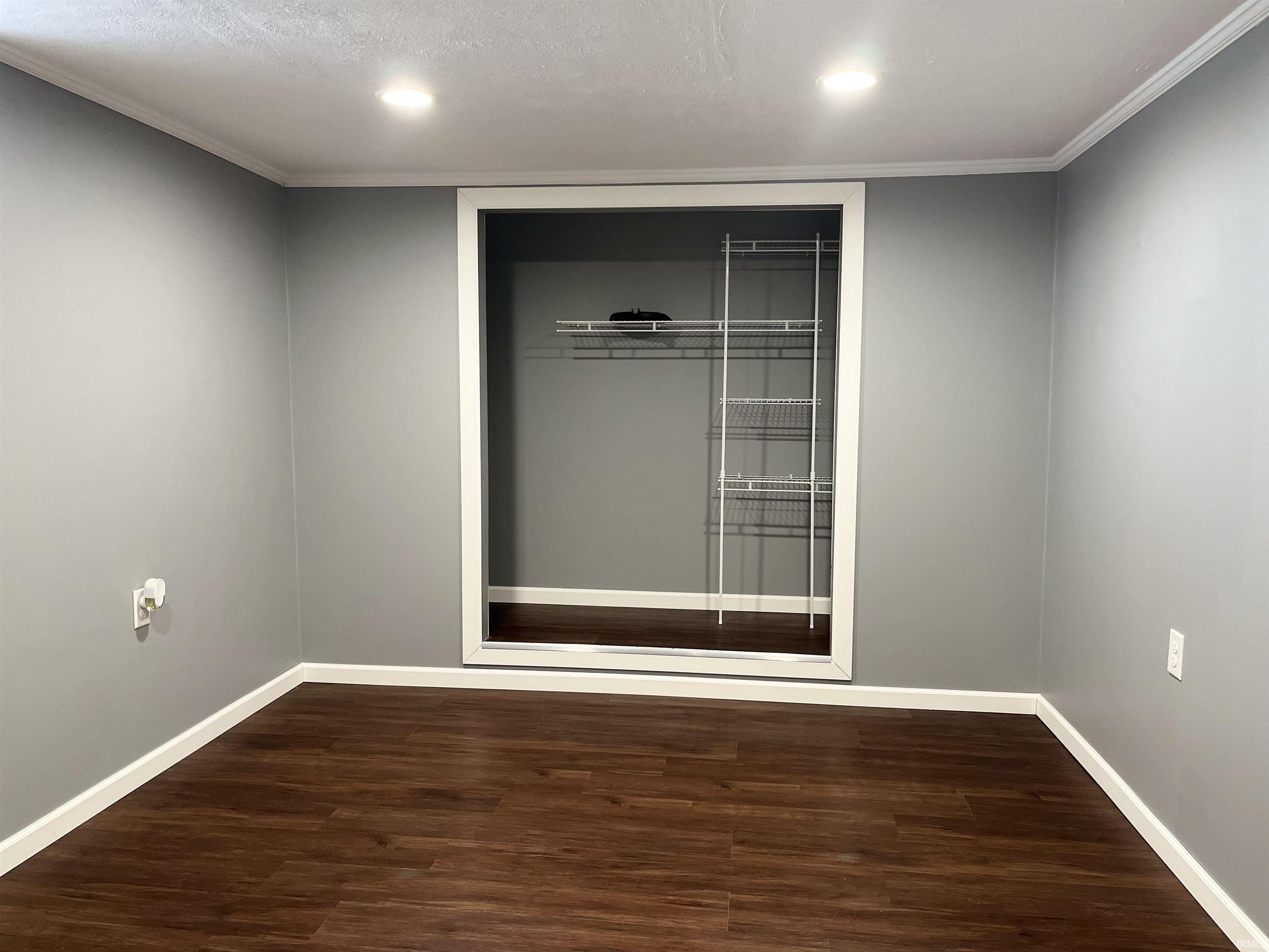 Spare room featuring dark wood-style floors, ornamental molding, and recessed lighting