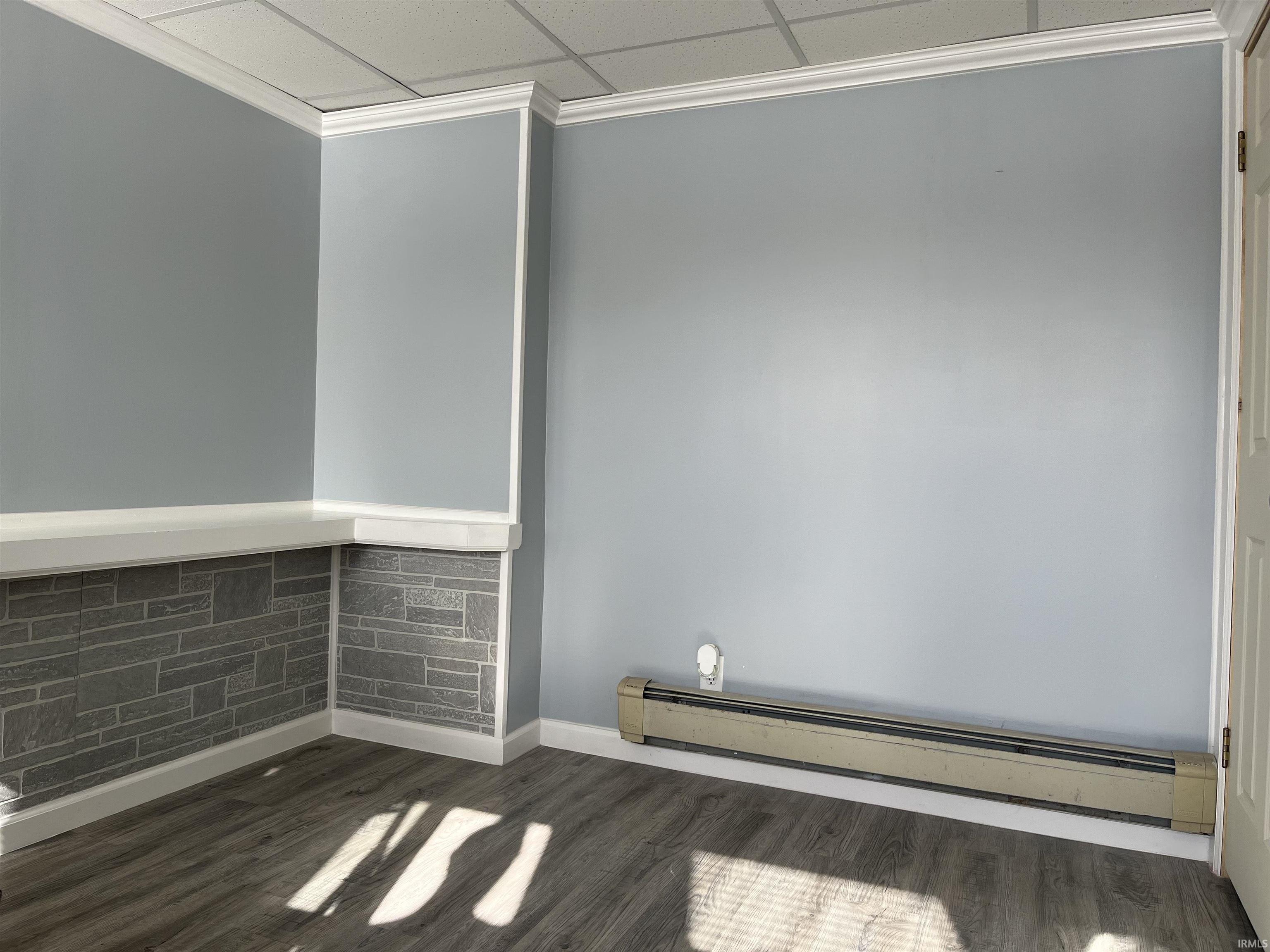 Empty room with a baseboard radiator, dark wood-style flooring, ornamental molding, and a drop ceiling
