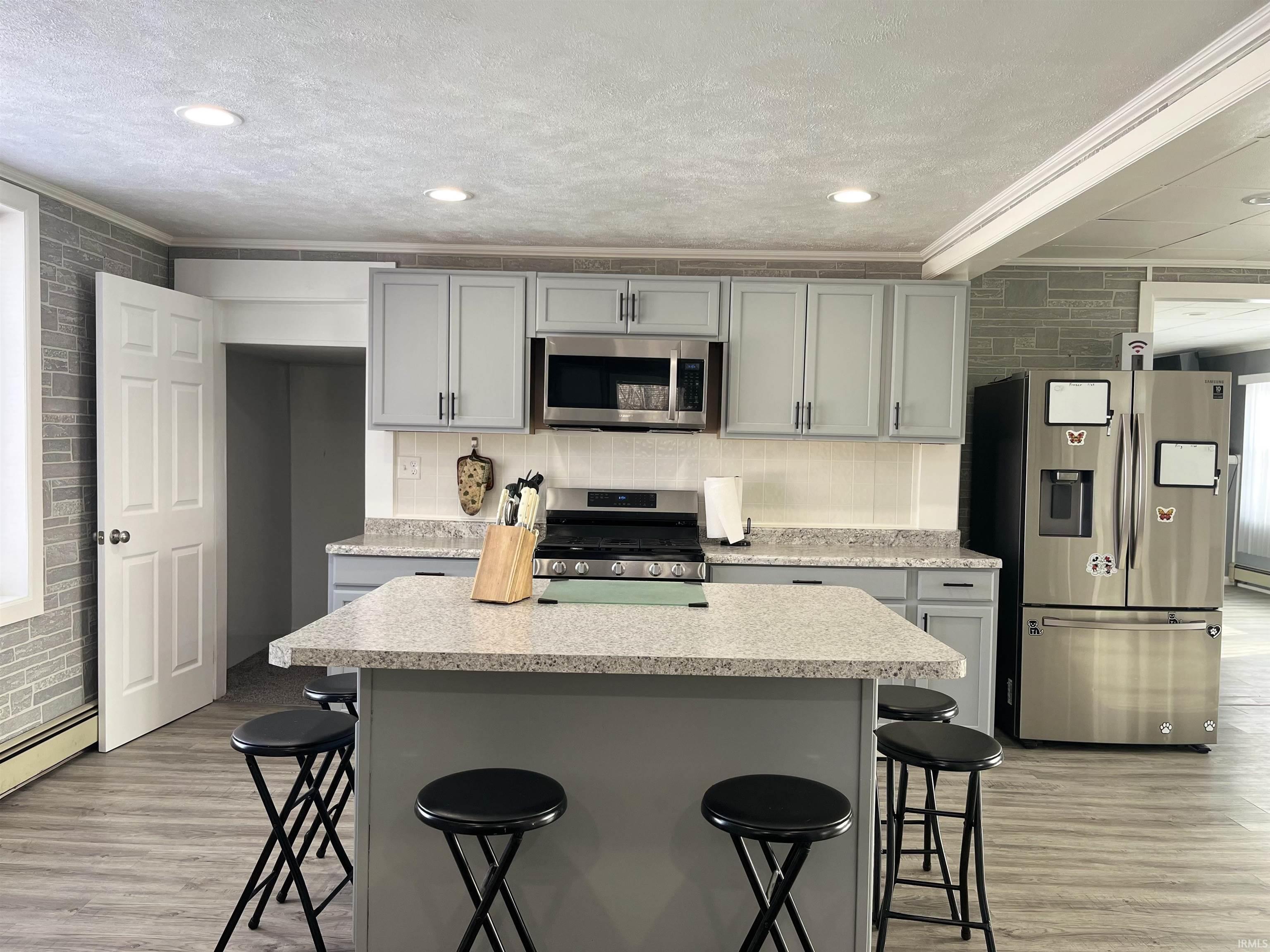 Kitchen featuring gray cabinetry, a kitchen bar, a center island, stainless steel appliances, and crown molding