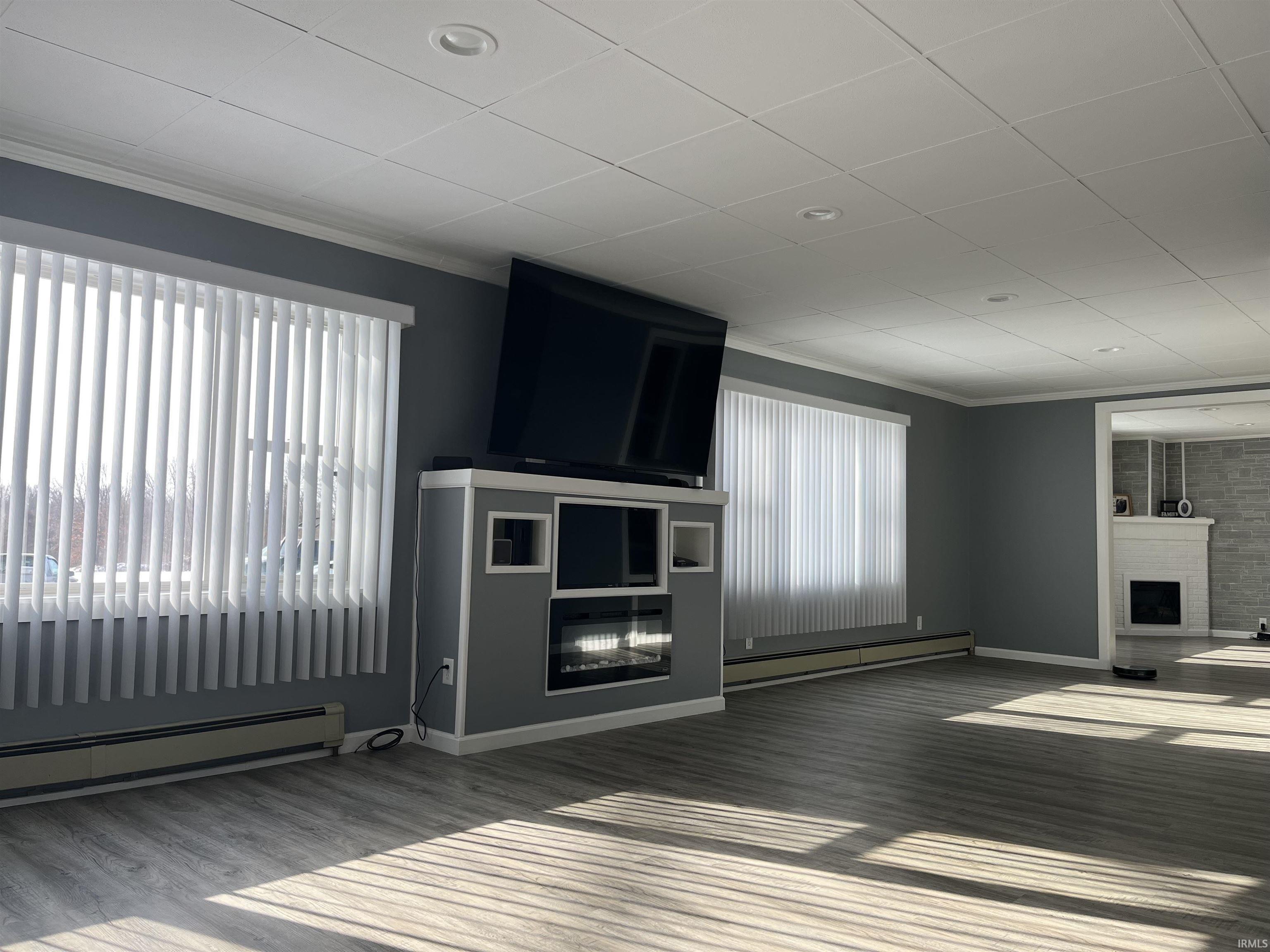 Unfurnished living room featuring a large fireplace, a baseboard heating unit, ornamental molding, wood finished floors, and a paneled ceiling