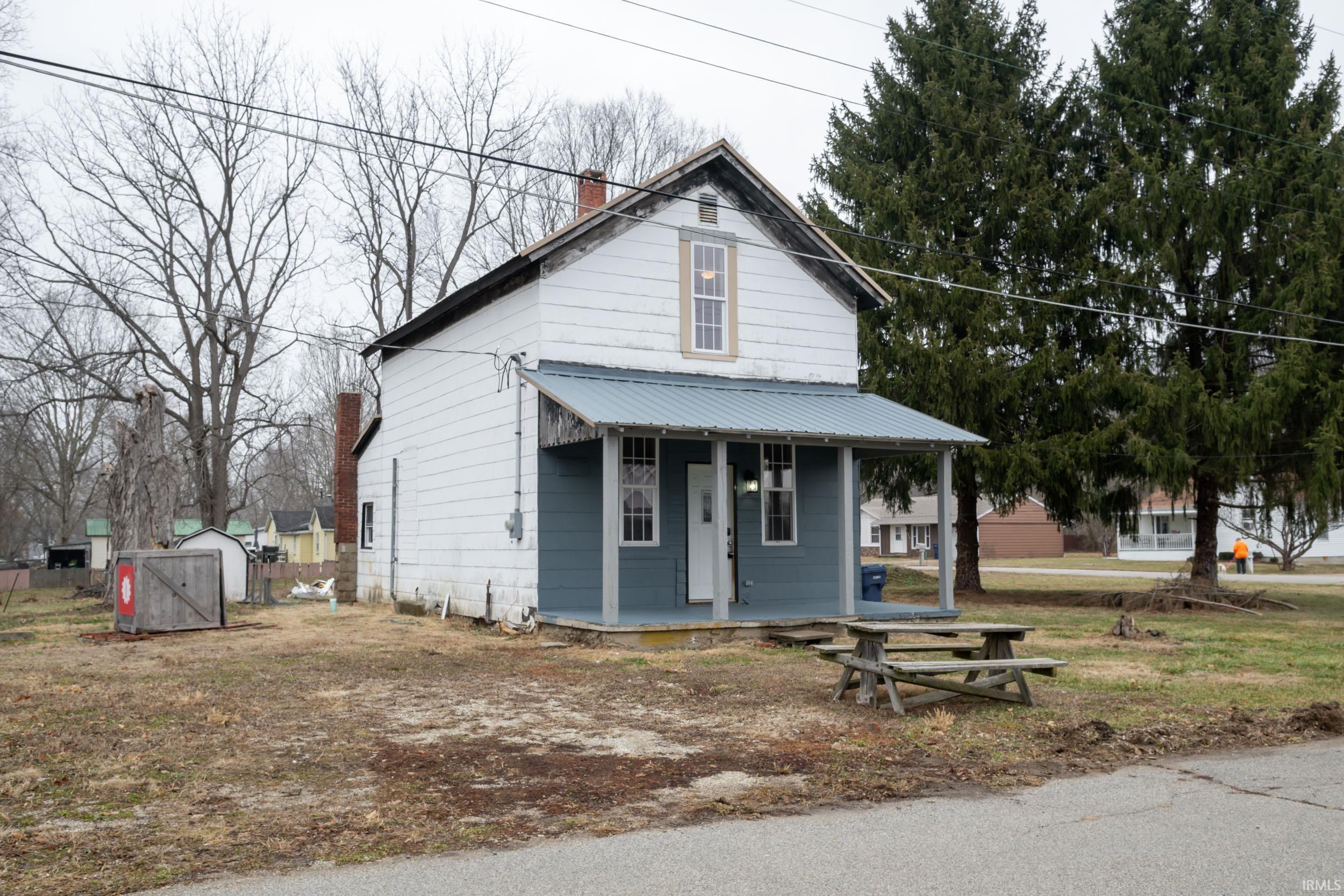 View of front of house featuring a porch, a chimney, a shed, and a metal roof