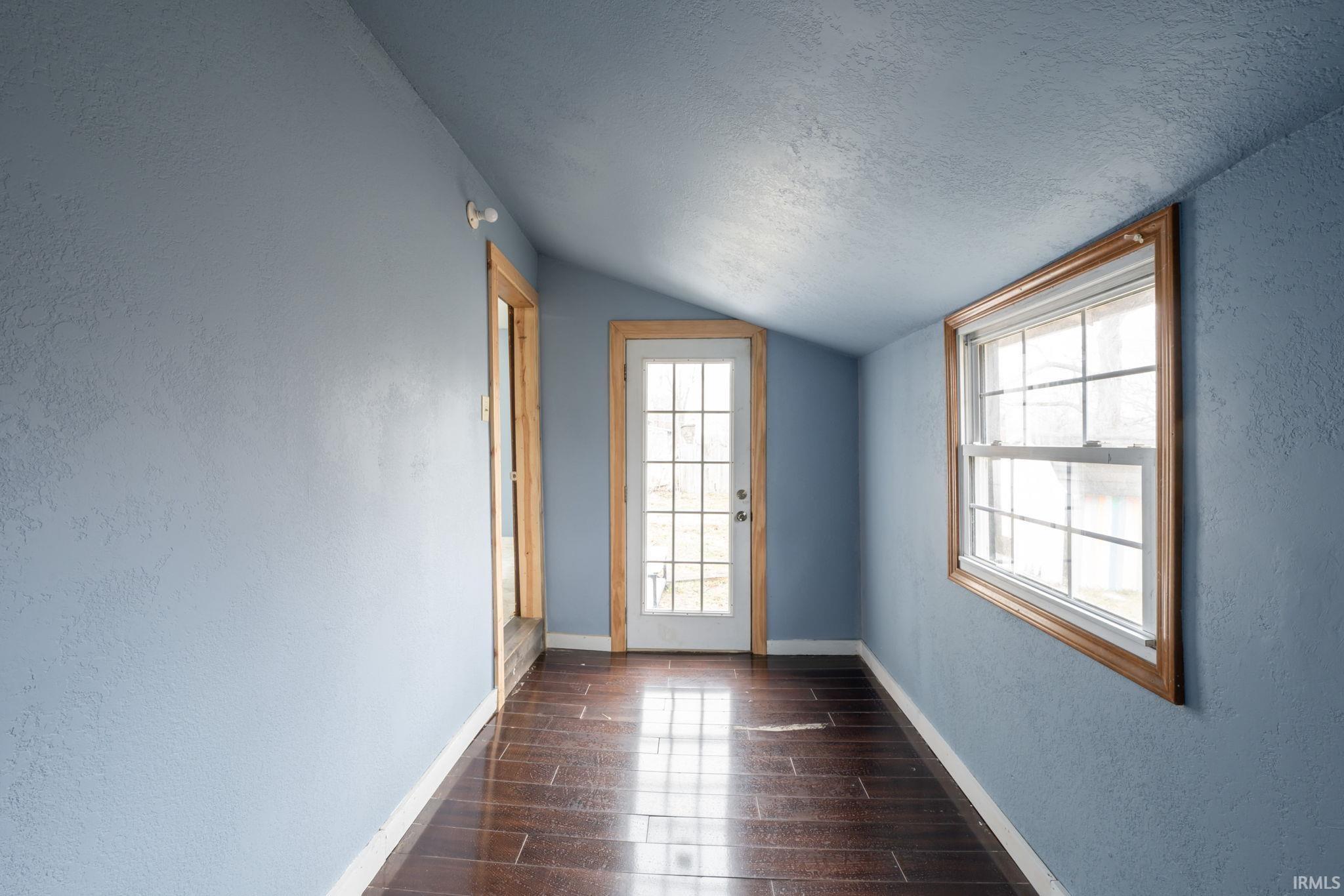 Spare room with a textured wall, a textured ceiling, dark wood-style flooring, and lofted ceiling