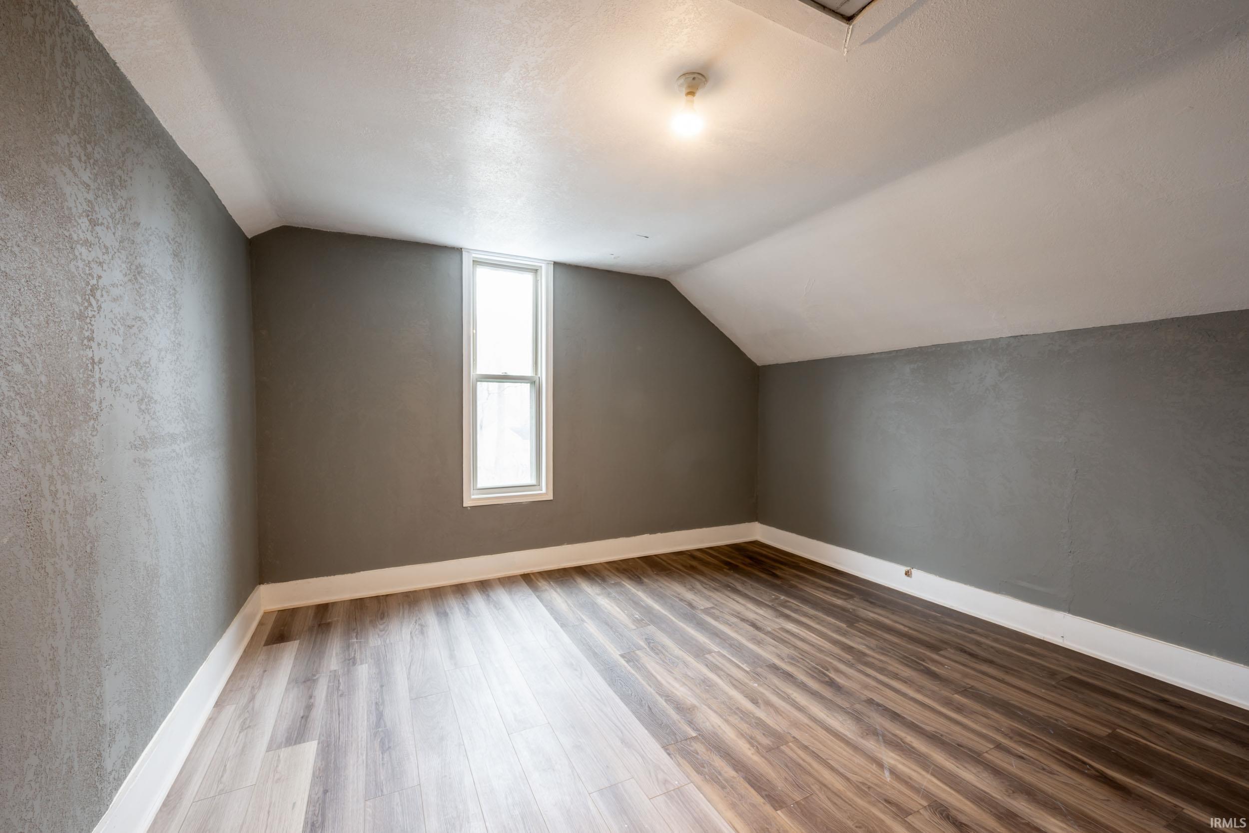 Additional living space with wood finished floors, lofted ceiling, and a textured ceiling