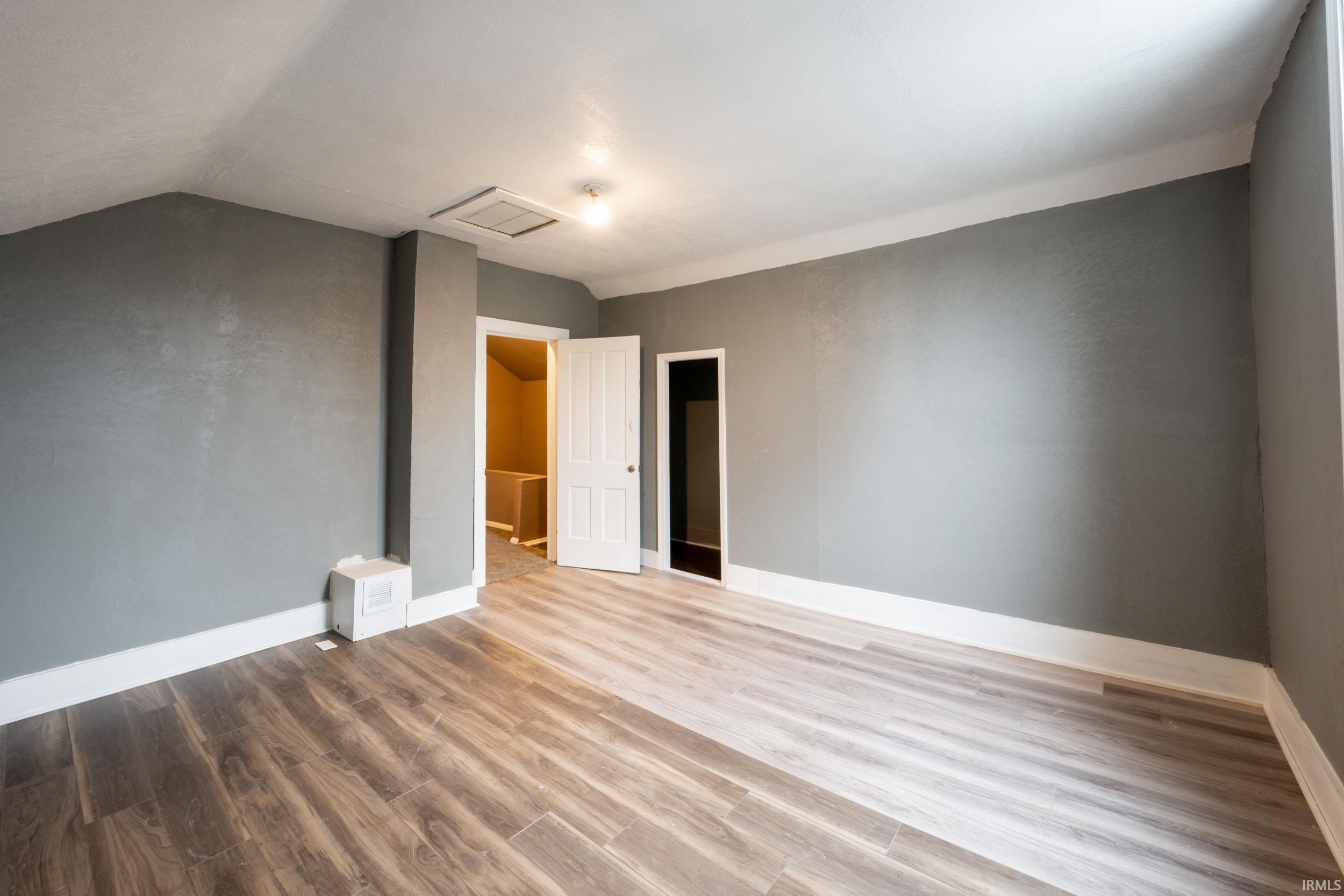 Unfurnished bedroom featuring wood finished floors and vaulted ceiling